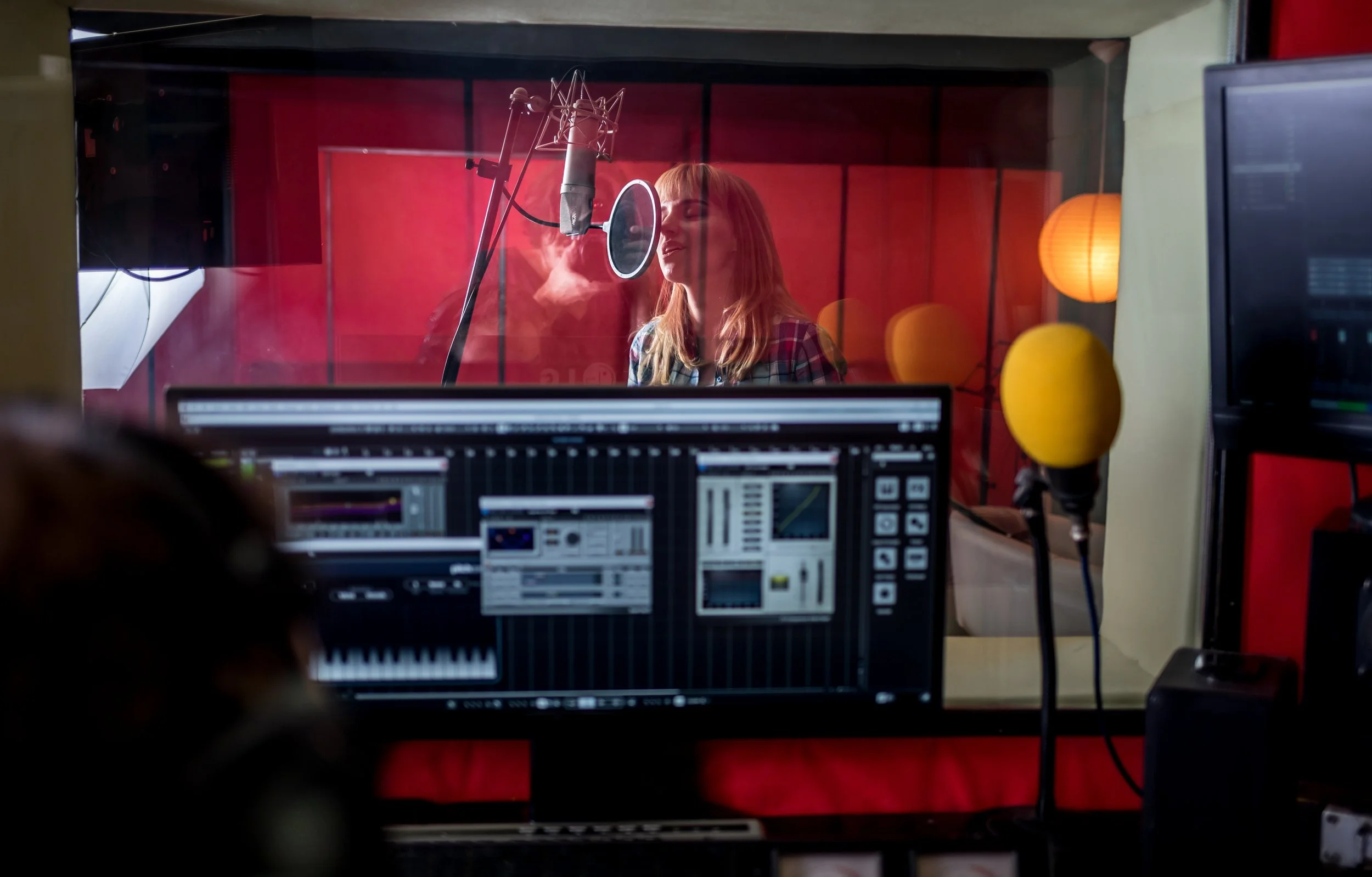 Mujer cantando en un estudio de grabación con micrófono y panel de control.
