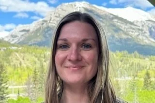 woman smiling with a snow-capped mountain and evergreens in the background