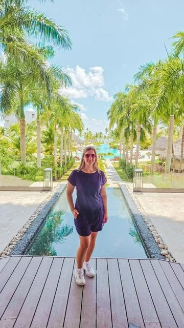 woman standing in front of a water feature in resort lobby with ocean and palm trees in the background