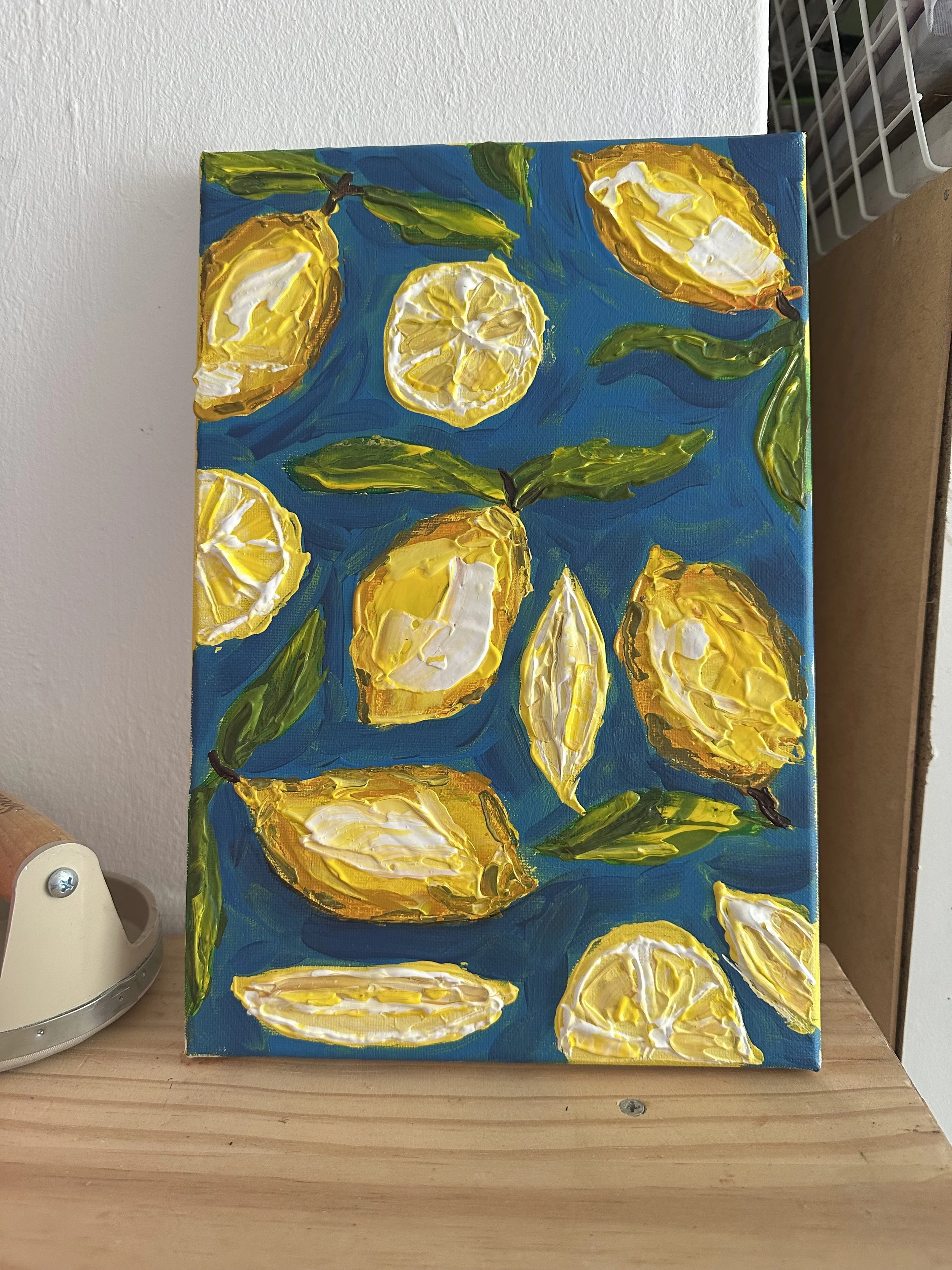 A colorful abstract painting of lemons, lemon slices, and green leaves on a blue background, created with thick textured brushstrokes.