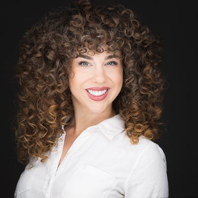 Portrait of a woman with curly hair smiling against a black background.