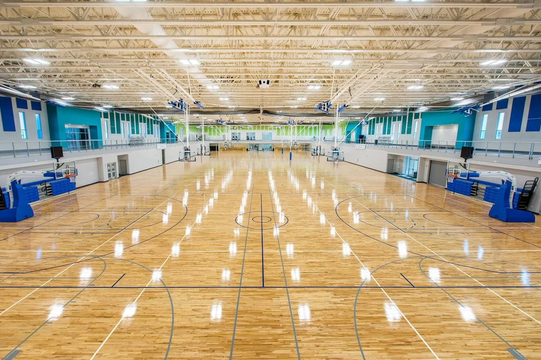 Empty indoor basketball court with polished wooden floor, multiple hoops, and colorful wall accents.