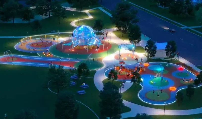 A brightly lit nighttime playground featuring a large glass-domed structure, colorful pathways, and several play areas with lights and equipment.