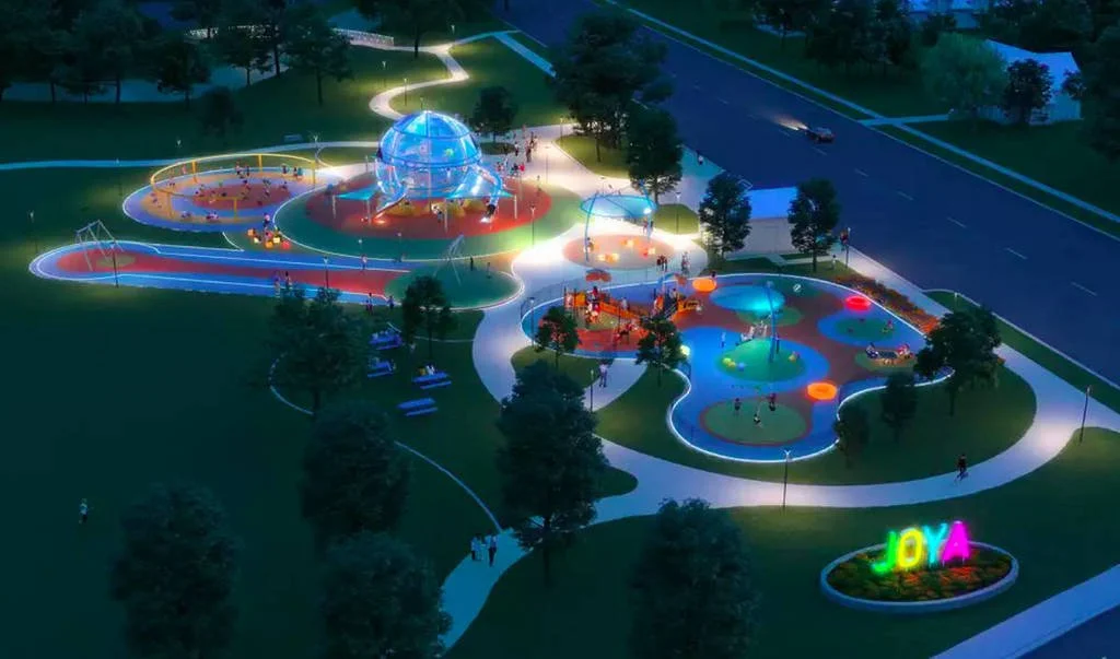 A brightly lit nighttime playground featuring a large glass-domed structure, colorful pathways, and several play areas with lights and equipment.