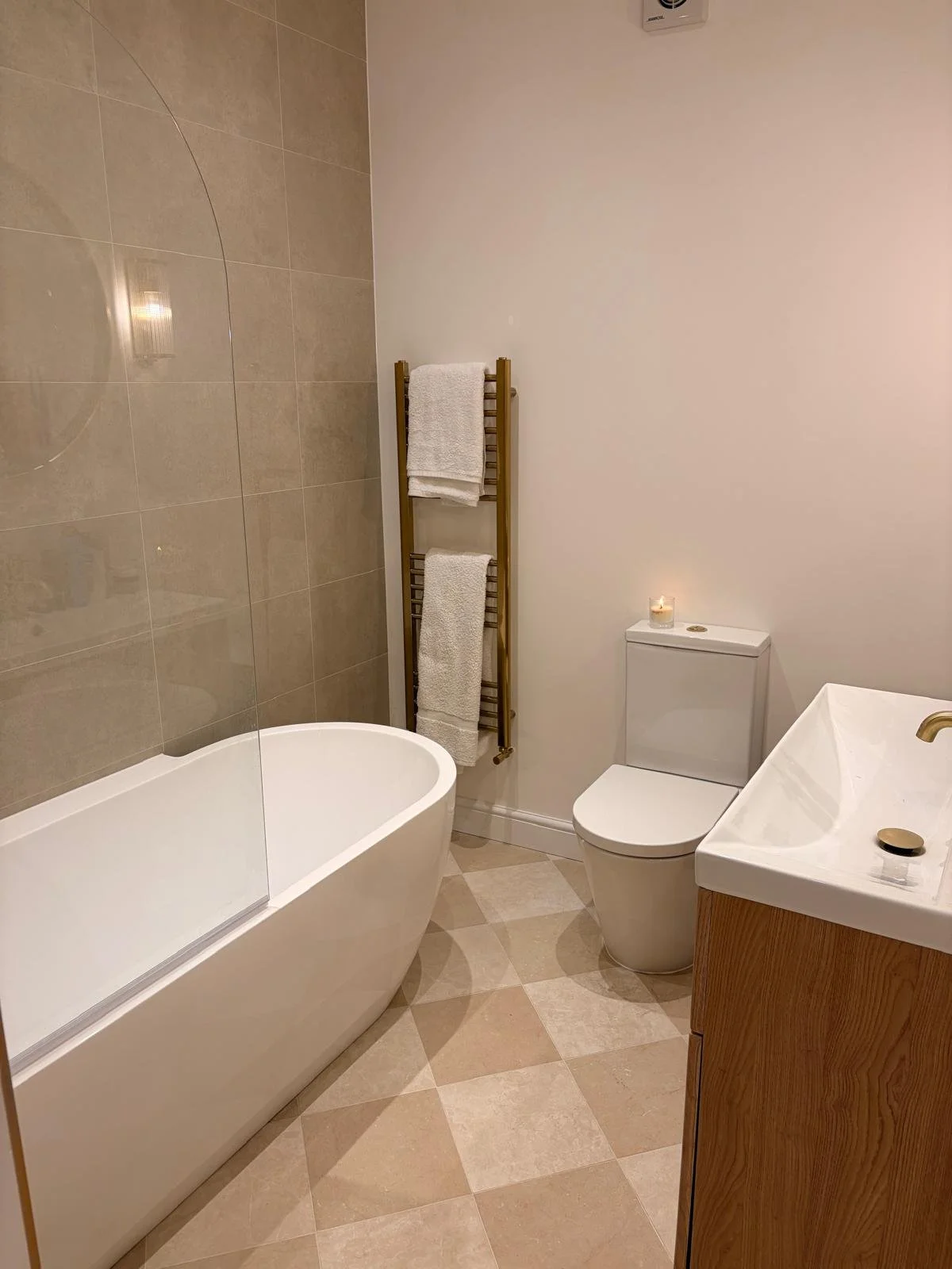 Modern bathroom with bathtub, shower, toilet, and sink, beige tiled walls, gray cabinets, window, and towel radiator.