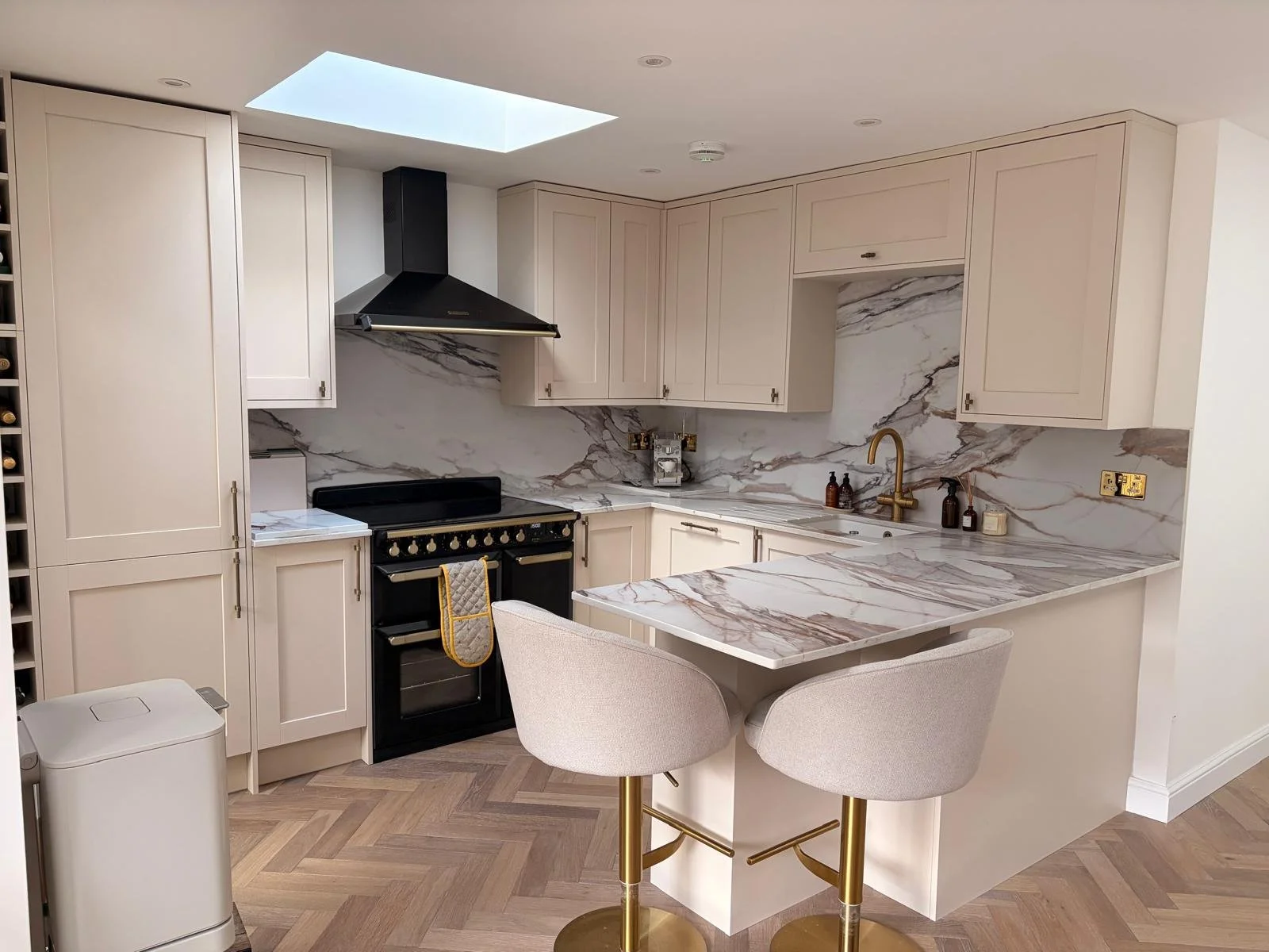 Modern kitchen with white cabinets, patterned backsplash, and a breakfast bar with beige stools, decorated with flowers, artwork, and bottles on a gold cart.