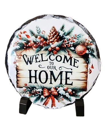 Decorative round sign with a Christmas theme, saying "Welcome to Our Home," surrounded by pinecones, holly, and a red ribbon, on a black background.