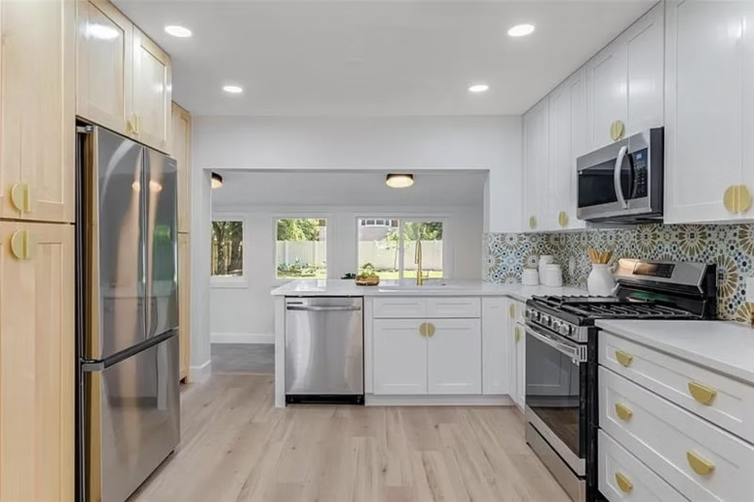 Modern kitchen with white cabinets, stainless steel appliances, colorful patterned backsplash, and light wooden floors.
