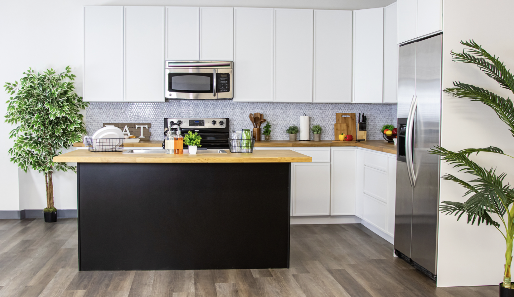 Modern kitchen with white cabinets, stainless steel appliances, black kitchen island with wood countertop, potted plants, and decorative items.