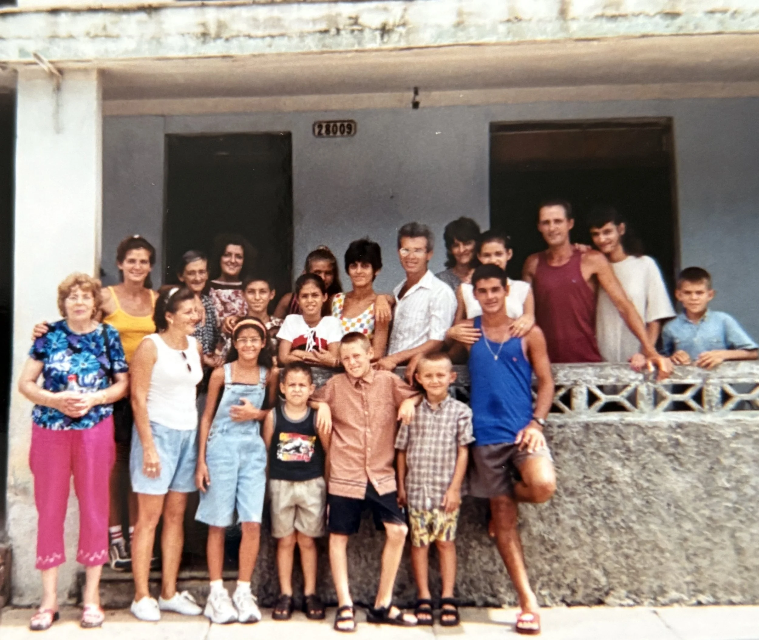 Group of children and adults posing together on the porch of a house, smiling for a photograph.