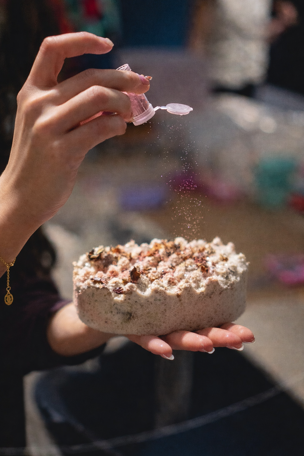 Person sprinkling colorful glitter over a cake.