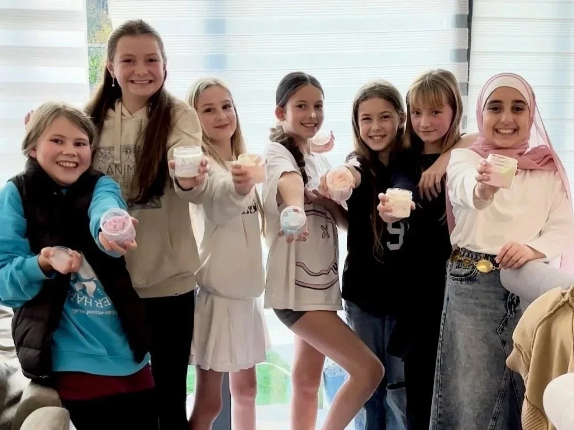 Group of seven girls smiling and holding cups of colourful whipped soap that they have made at a Bath & Body Party in Sussex, hosted by Brighton Rock Workshop
