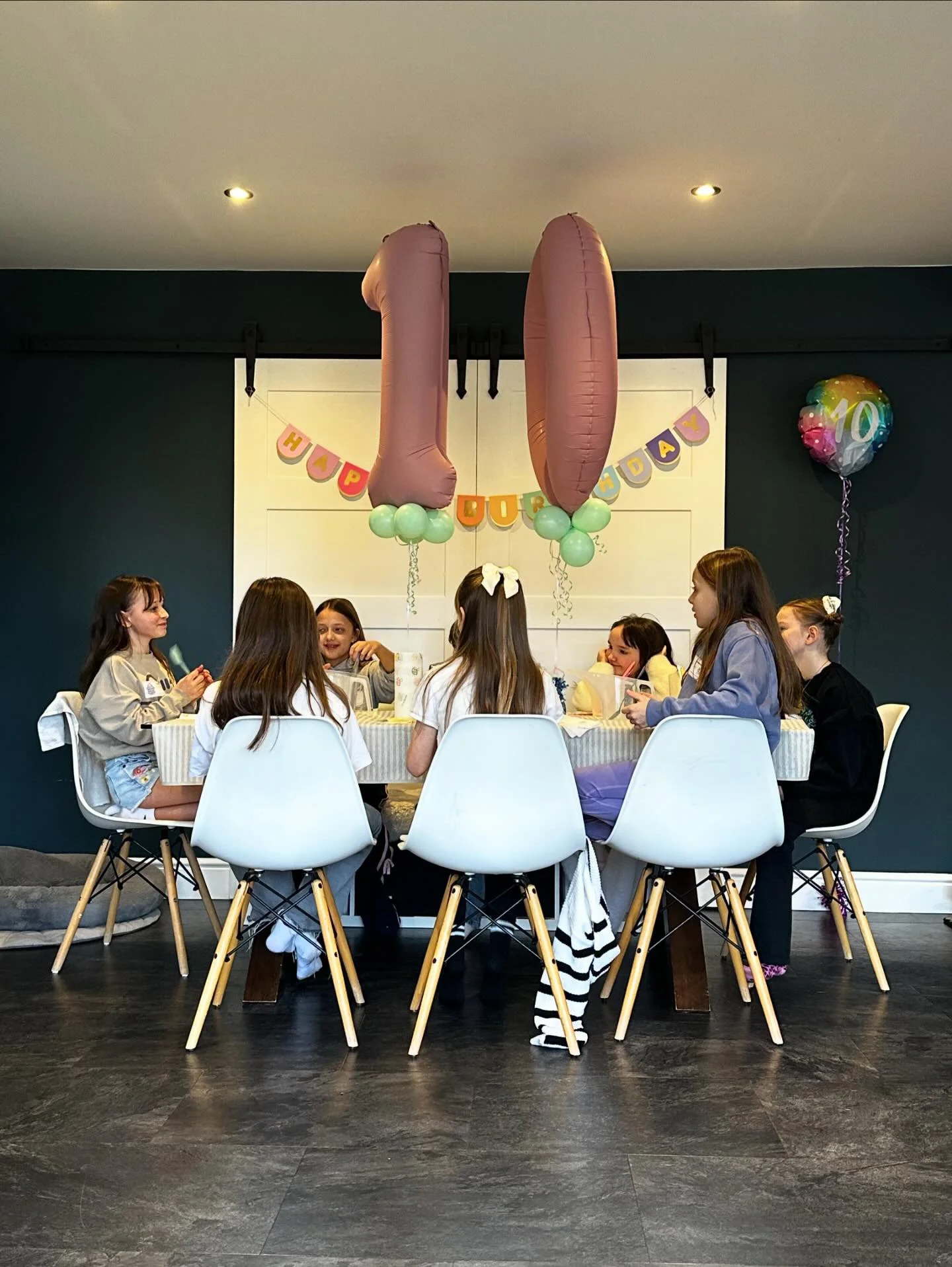 Children gathered around a table celebrating a birthday party with balloons, including a large '10' balloon, and a colorful 'HAPPY BIRTHDAY' banner behind them.