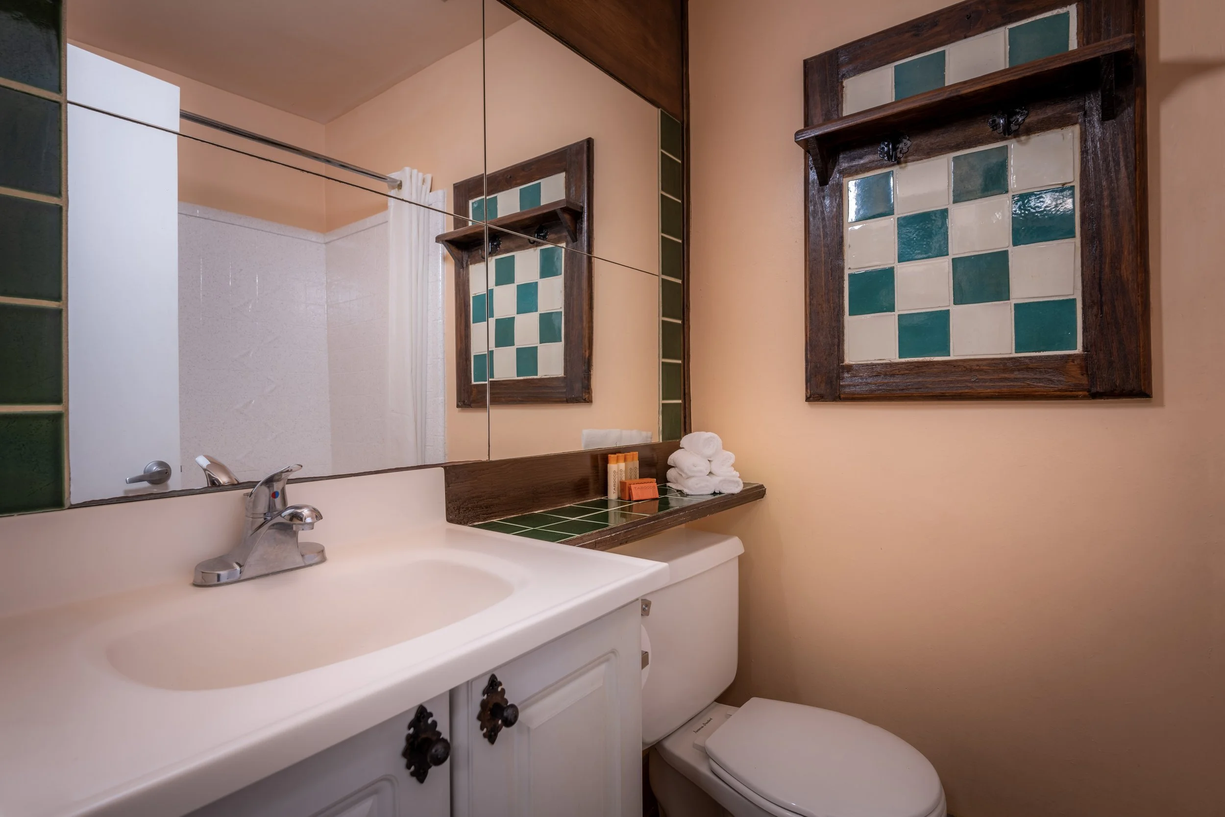 Bathroom sink with a mirror, towels, soap, and decorative tile framed artwork on peach walls.