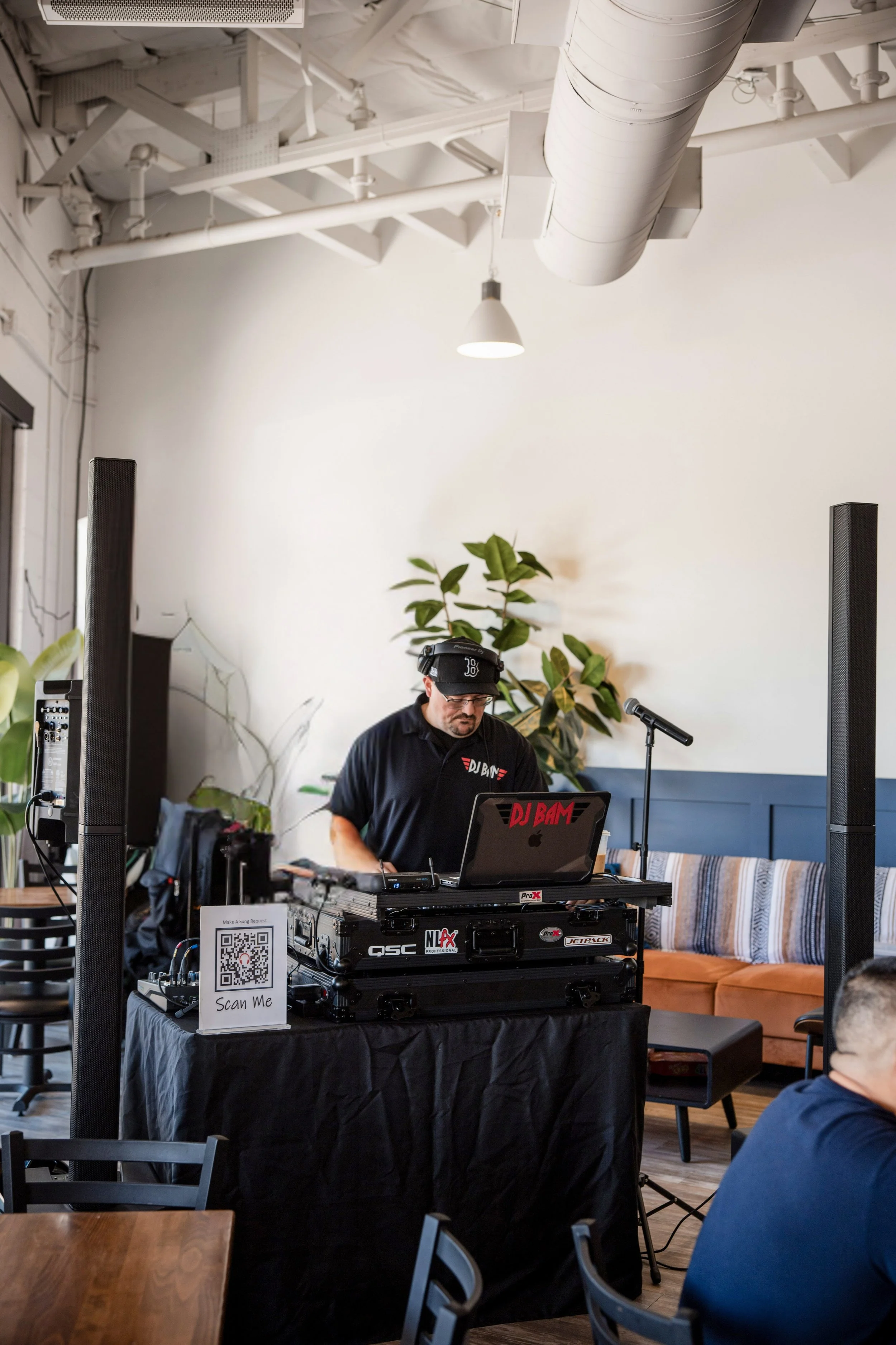 DJ Bam performing live with professional DJ setup at an indoor Arizona event venue.  Modern sound equipment and interactive QR code display enhance guest experience.  Inclusive Entertainment DJ service for weddings, parties, and corporate events.