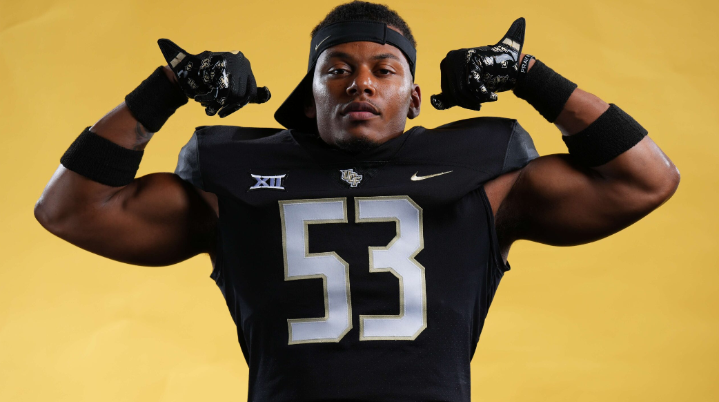 An American football player wearing a black uniform with gold and white accents, flexing his biceps, against a yellow background.