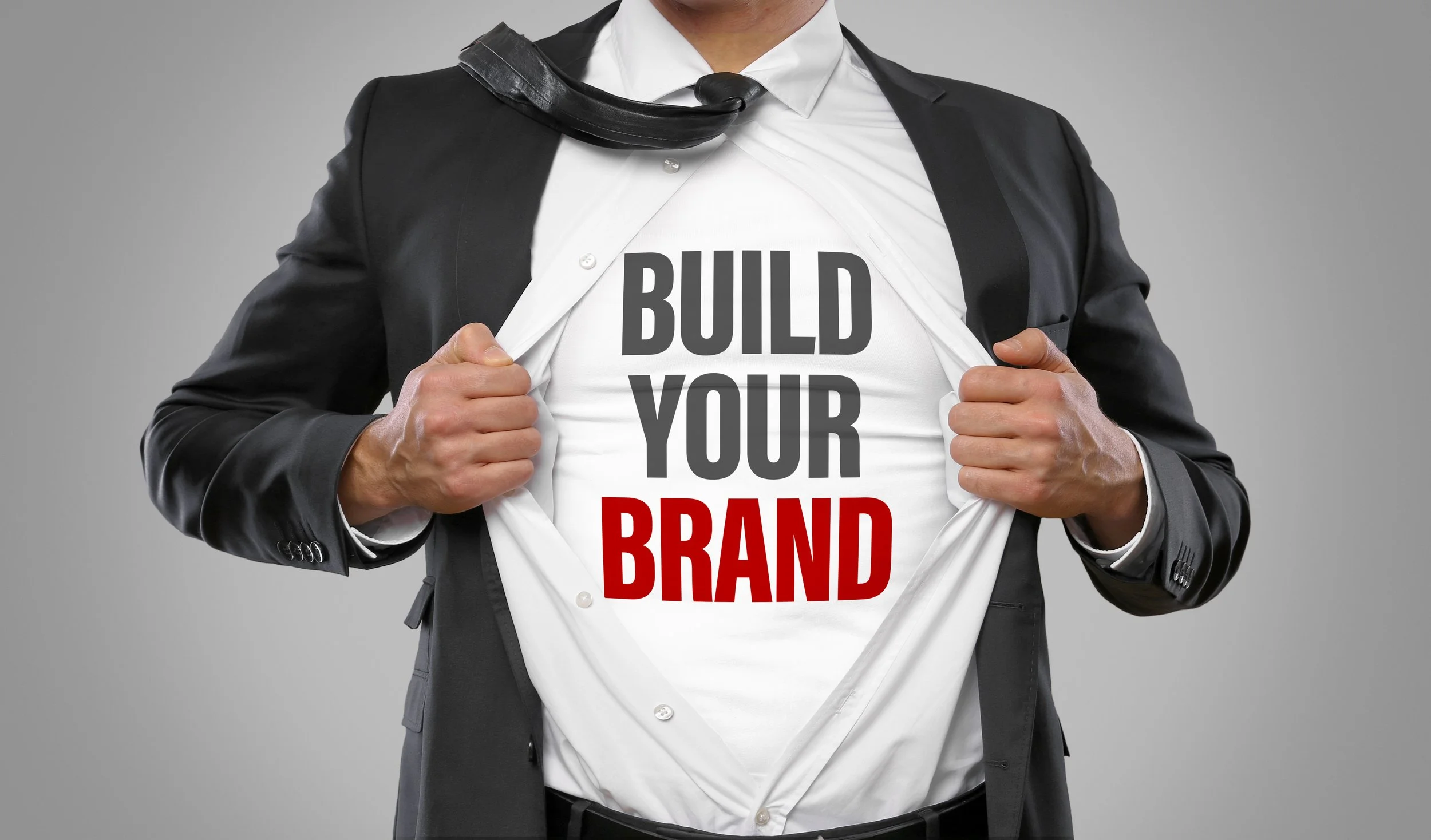 A man in a suit opening his shirt to reveal a T-shirt underneath with the text 'Build Your Brand' in bold letters.