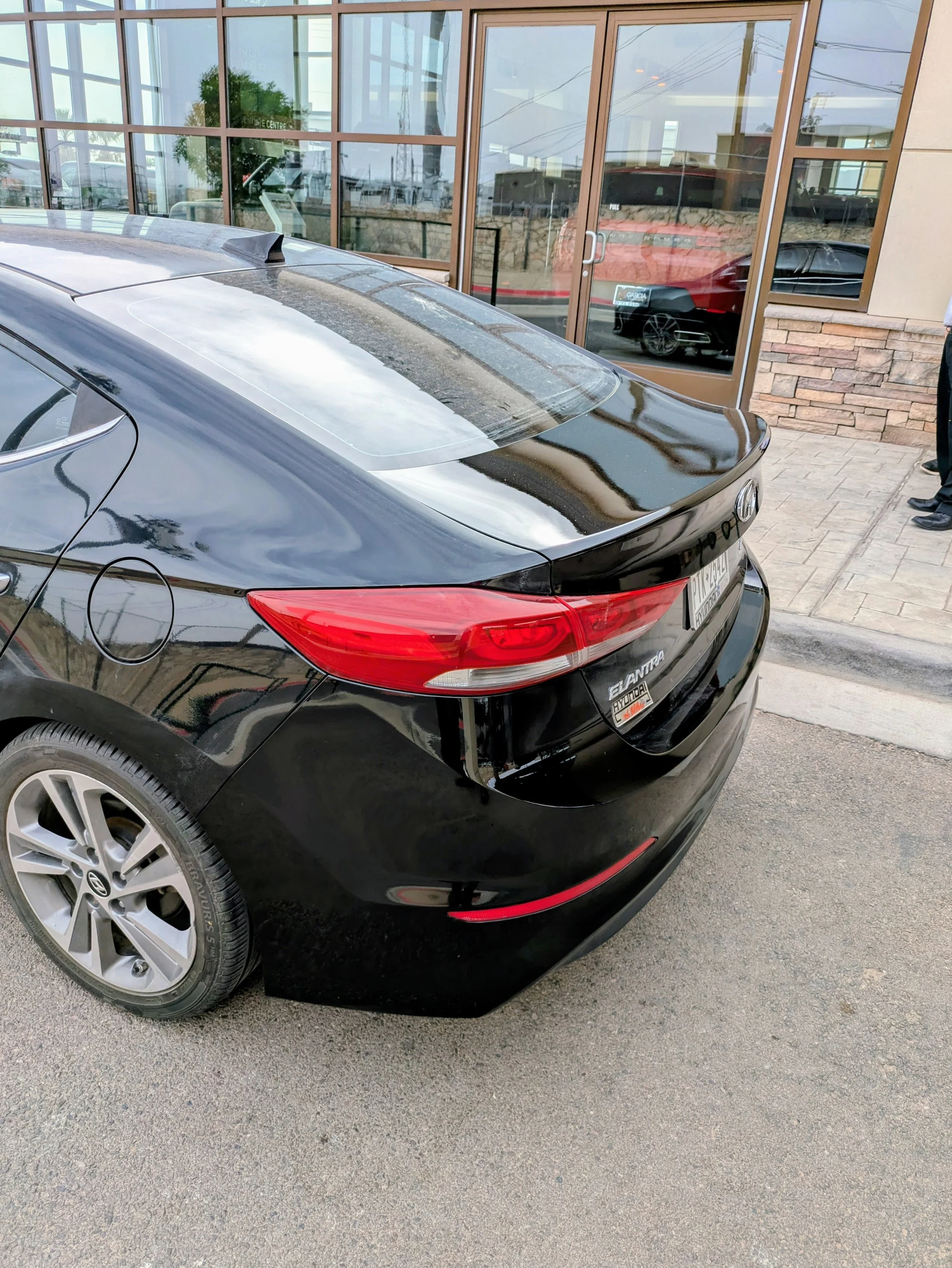 Black Hyundai Elantra parked outside a building with glass windows and a brick facade.