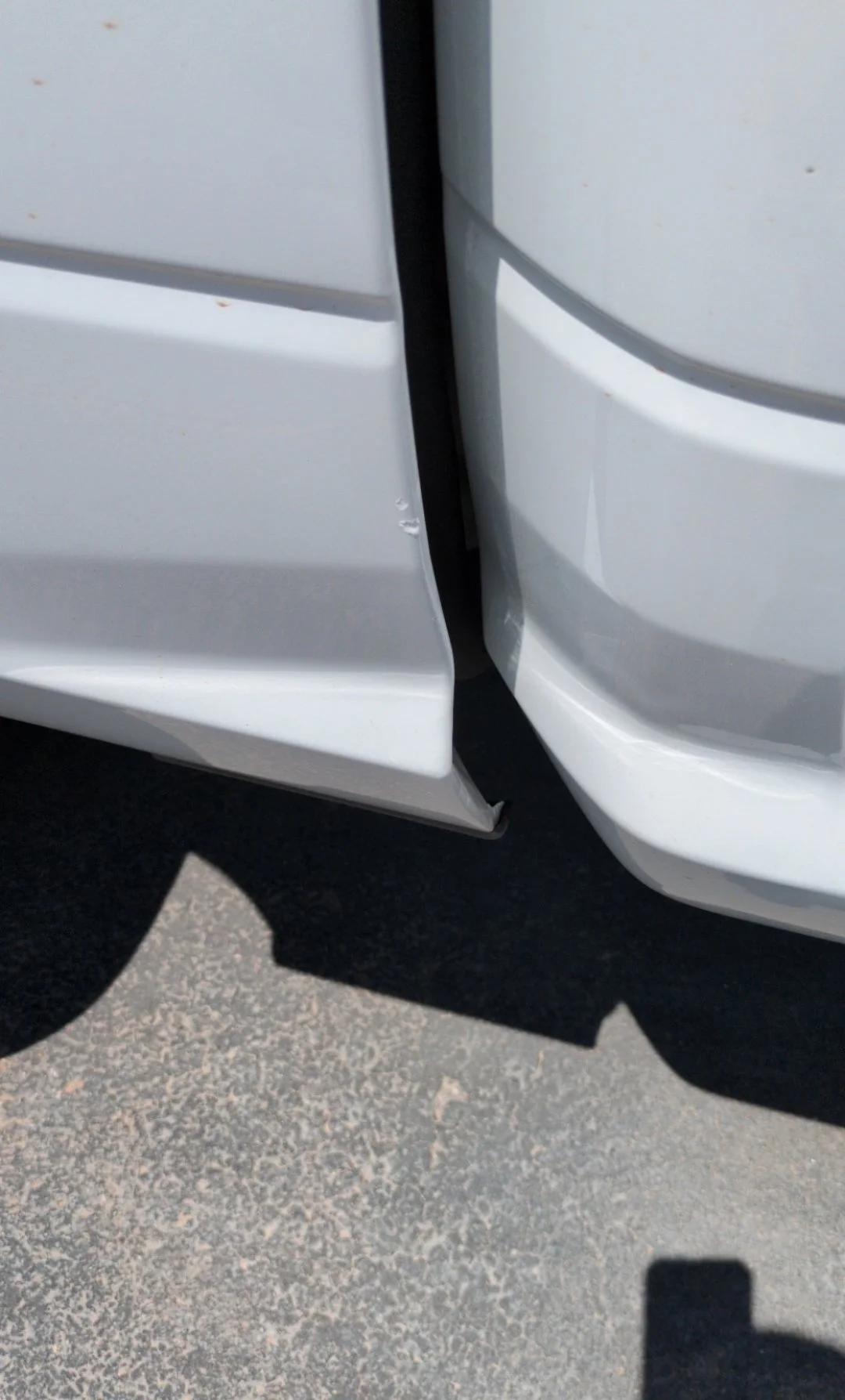 Close-up of a white vehicle's front bumper and side, showing a small dent and a slight misalignment between the panels.