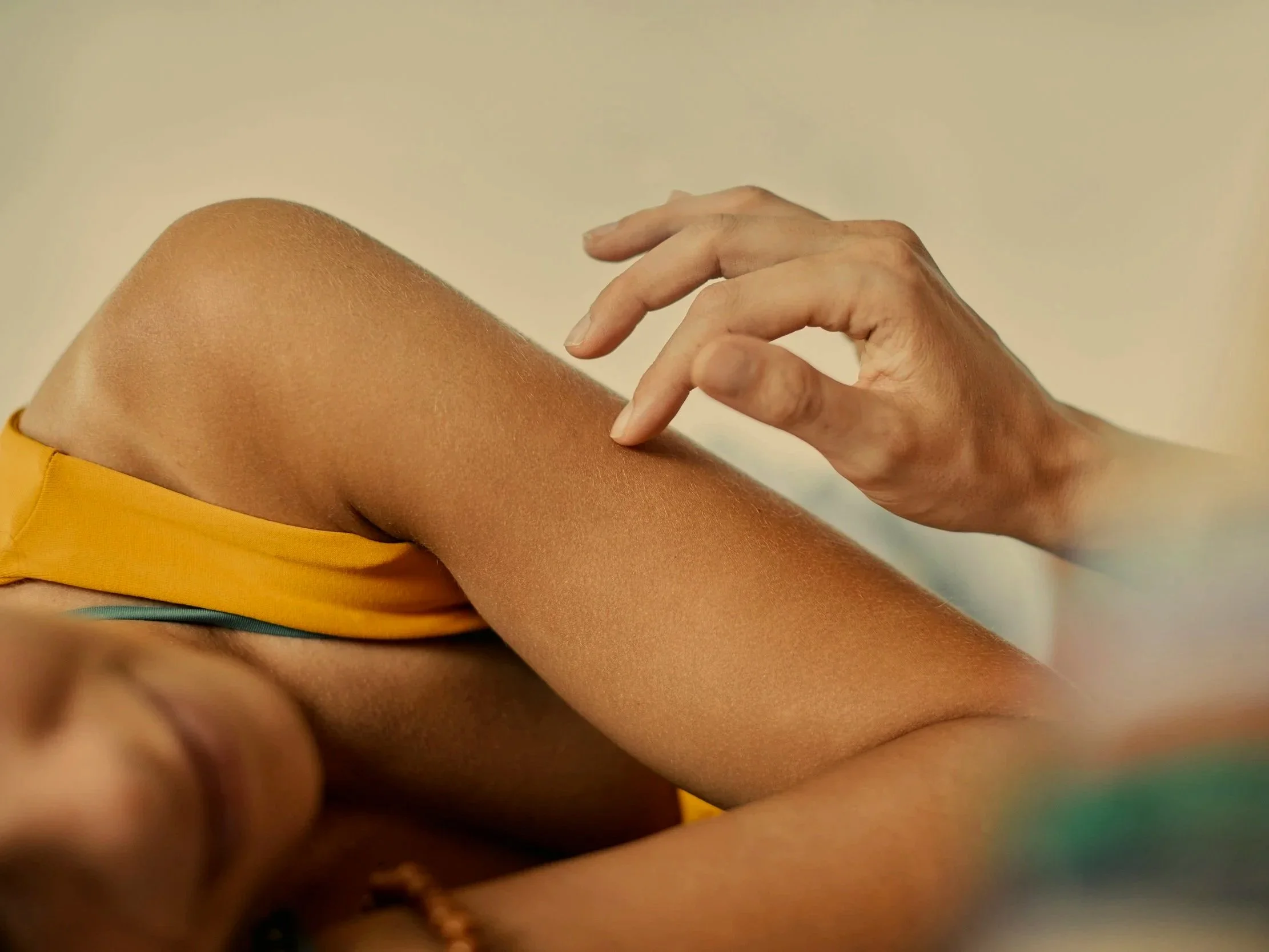 Close-up of a person's hand gently resting on their knee, with the skin tone of the leg and hand visible against a neutral background.