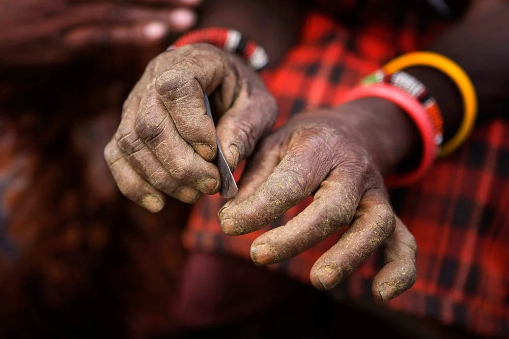Close-up of dusty hands holding a small metal tool, with a red and black plaid shirt in the background.