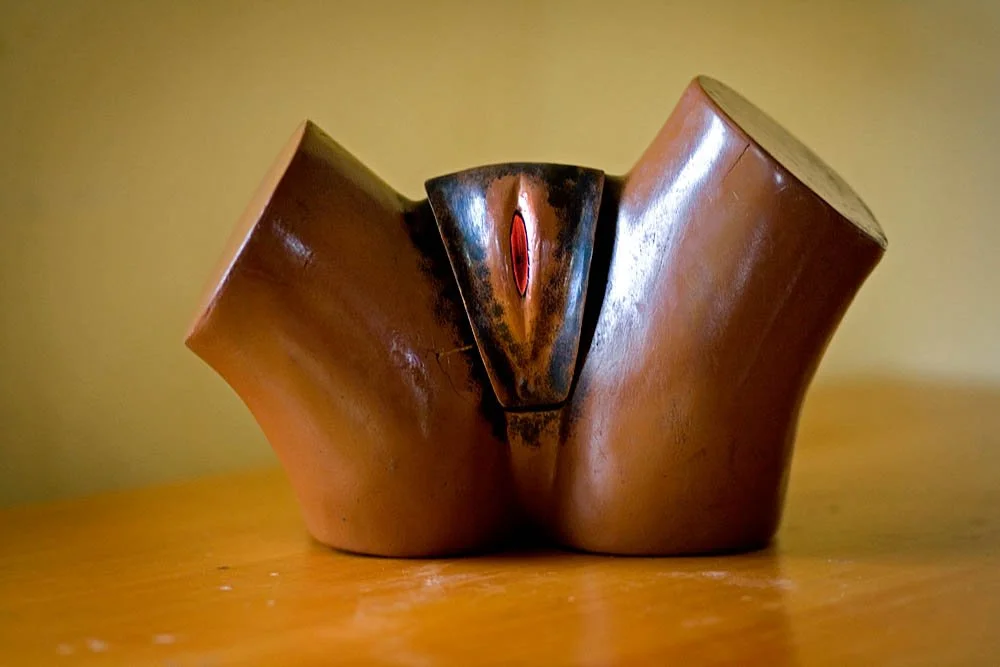 Abstract ceramic sculpture with curved, brown, and black sections on a wooden surface.