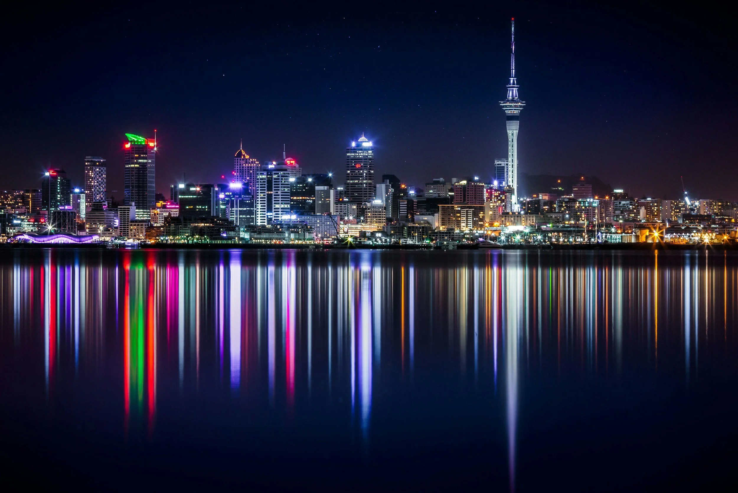Nighttime city skyline with illuminated buildings reflecting a connected city and reflections on calm water.