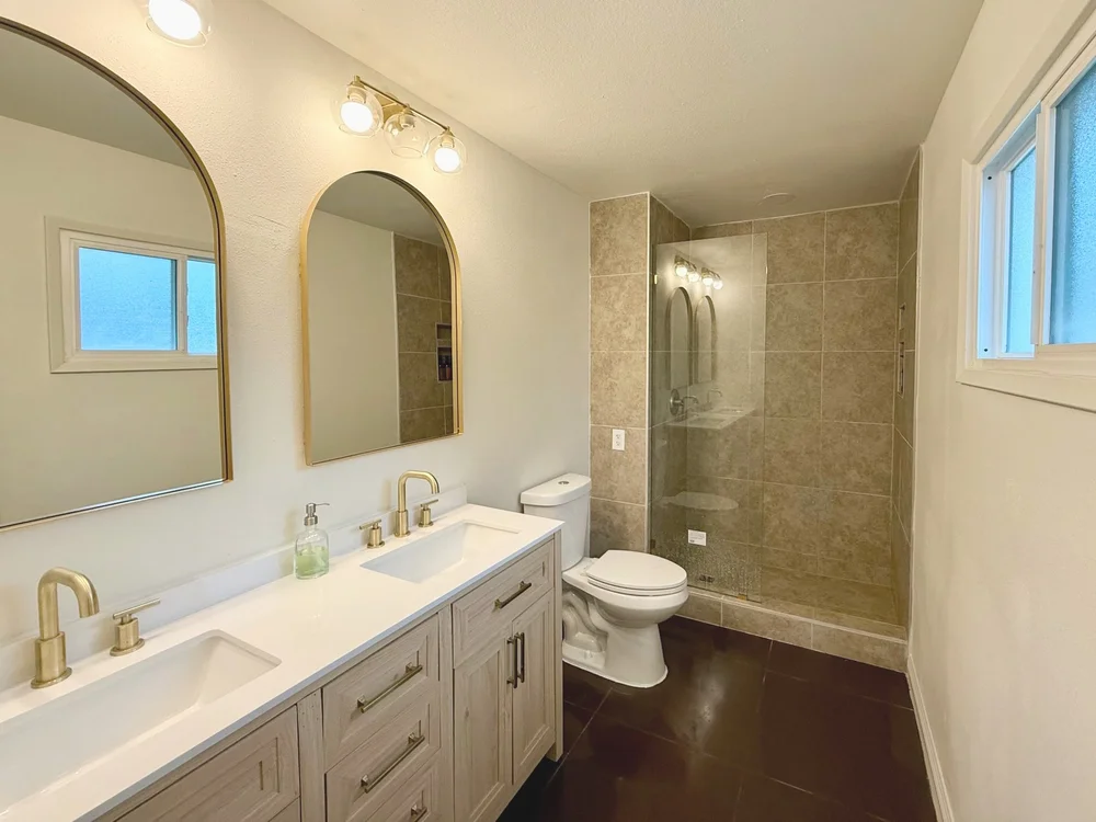 Remodeled bathroom with double vanity, arched mirrors and tiled shower
