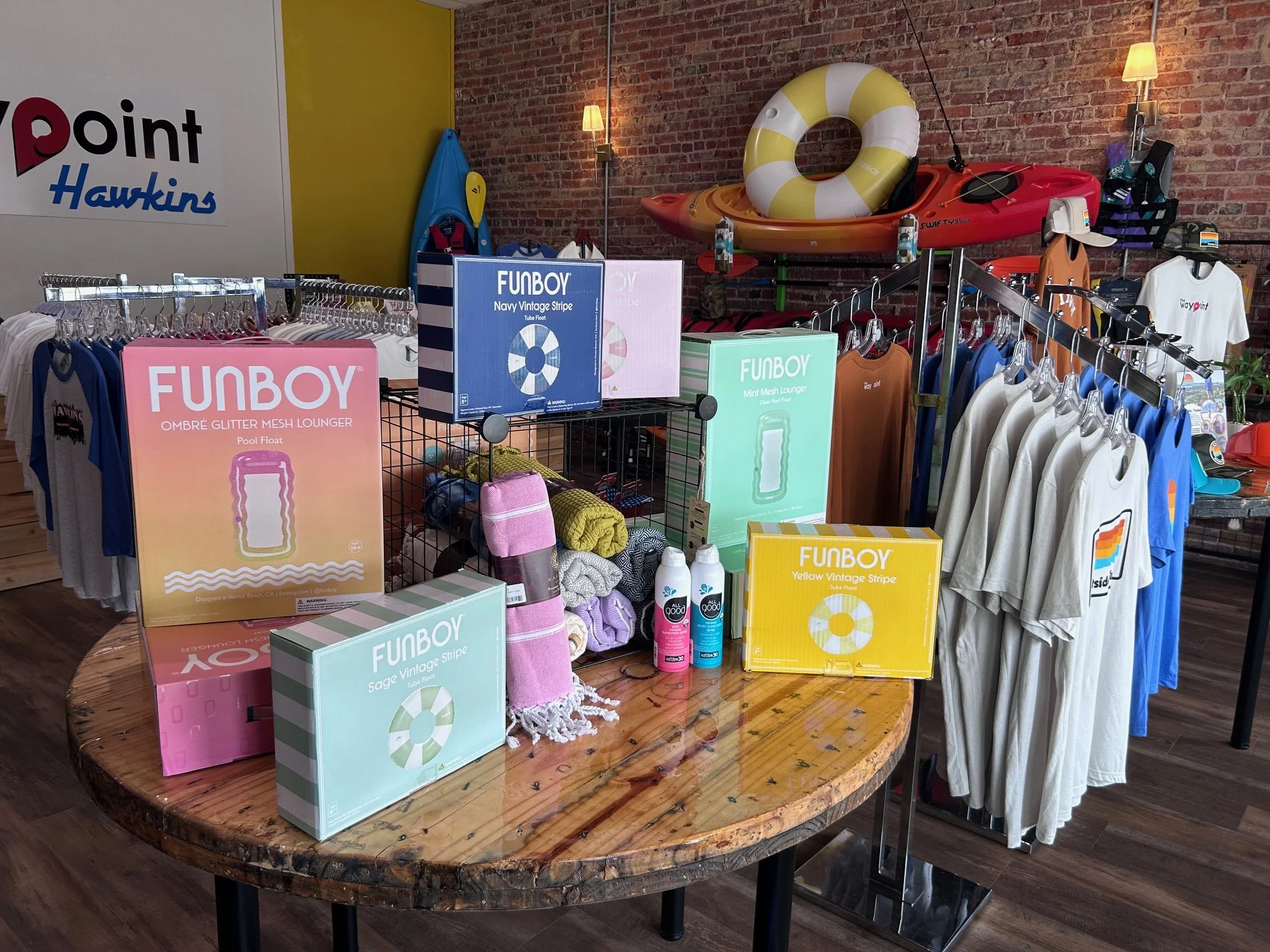 Display of Funboy mesh pool floats, towels, and accessories in a retail store with kayak and life preserver on wall.