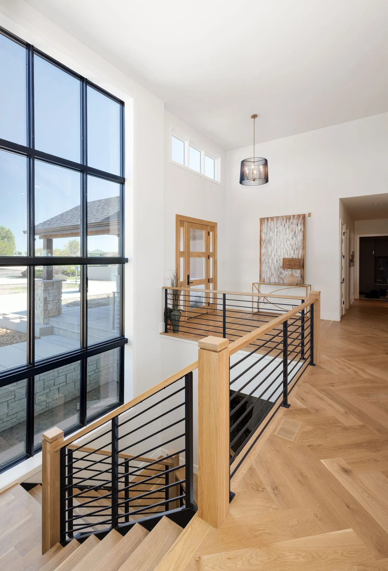 Interior of modern home with wooden staircase, large black framed windows, and white walls.