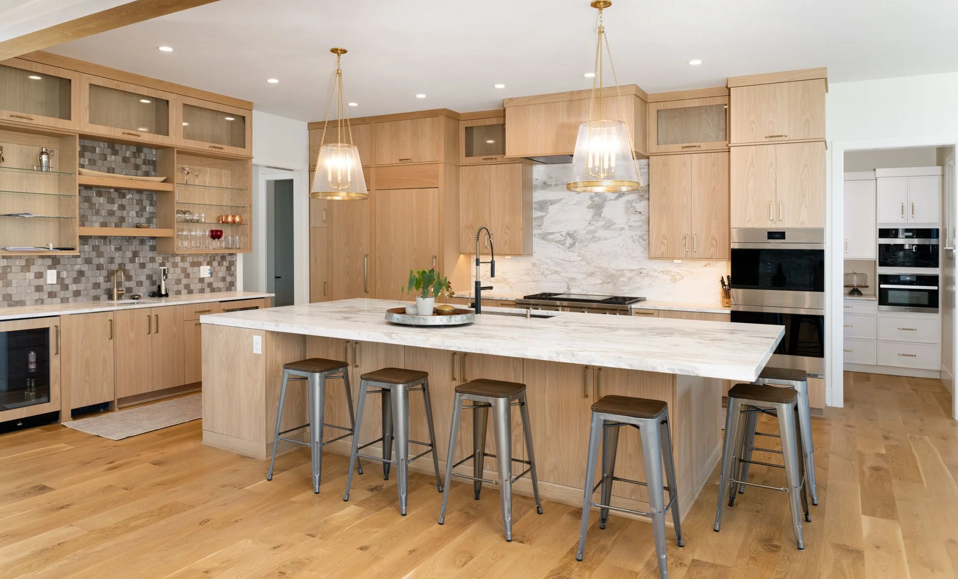 Modern kitchen with wooden cabinets, marble countertops, a kitchen island with seating, hanging pendant lights, and stainless steel appliances.