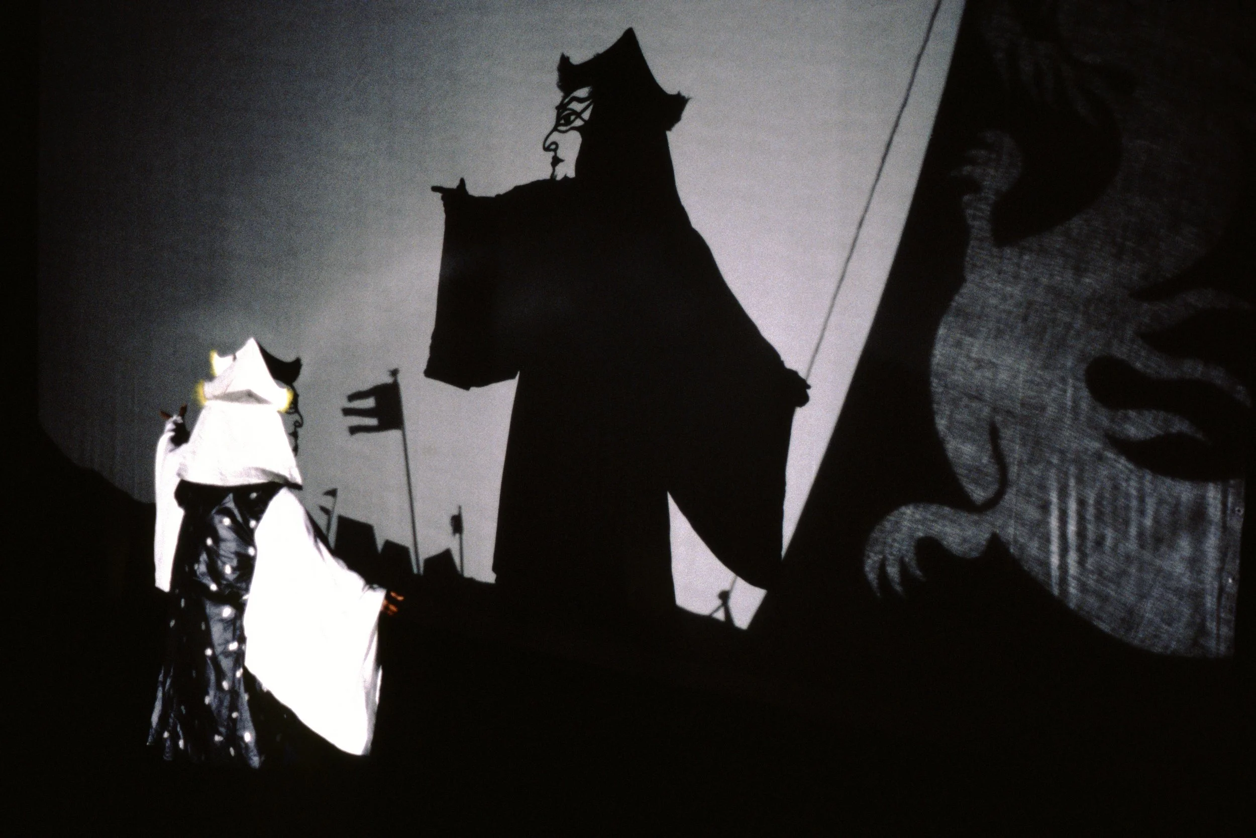 Silhouettes of medieval figures with flags, set against a backdrop of banners with a woman's face, all in black and white.