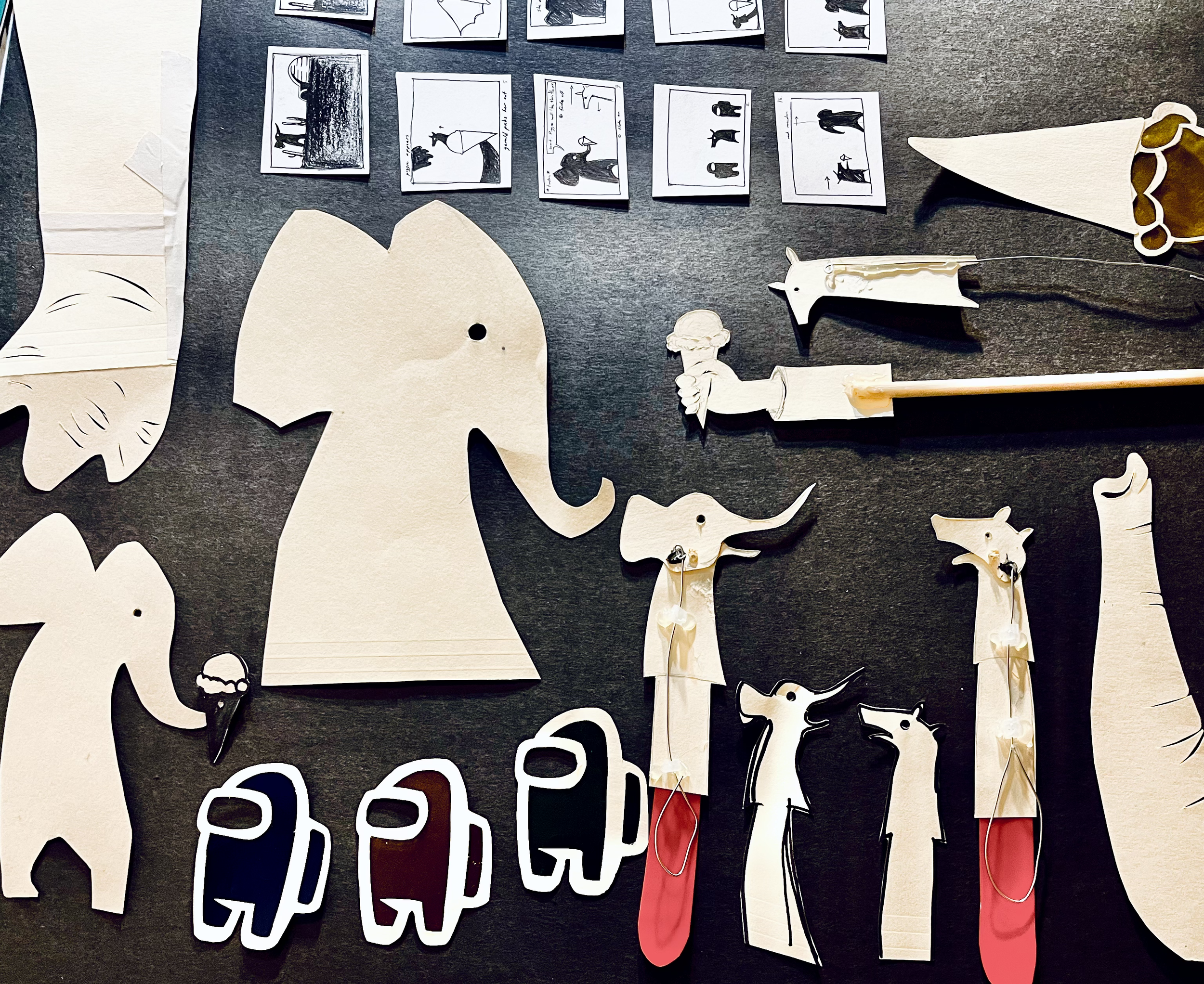 Paper crafts of elephants along with small illustrated story panels arranged on a black surface.