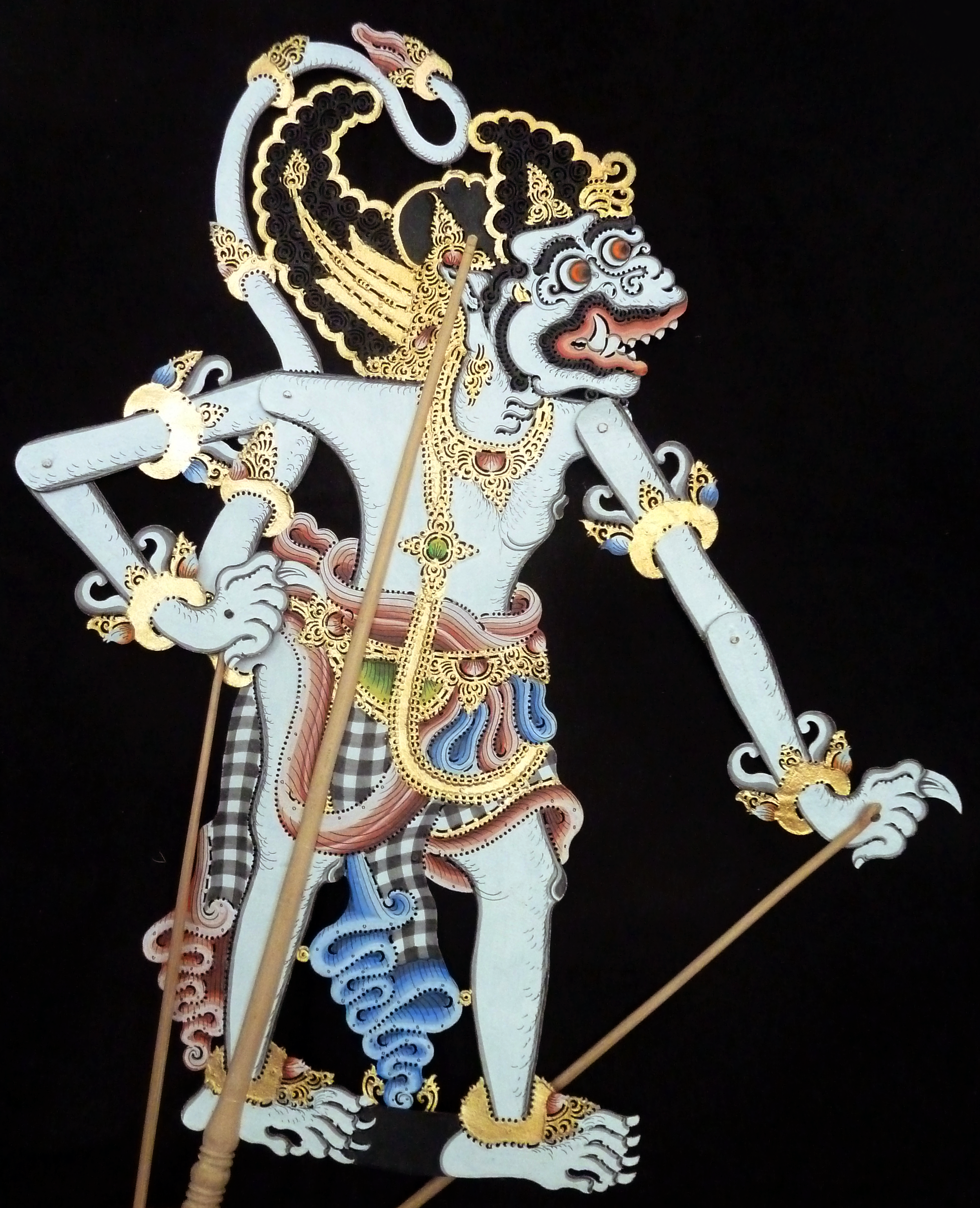 Decorative traditional shadow puppet of a fierce mythological creature with detailed gold, black, white, and colored patterns, set against a black background.