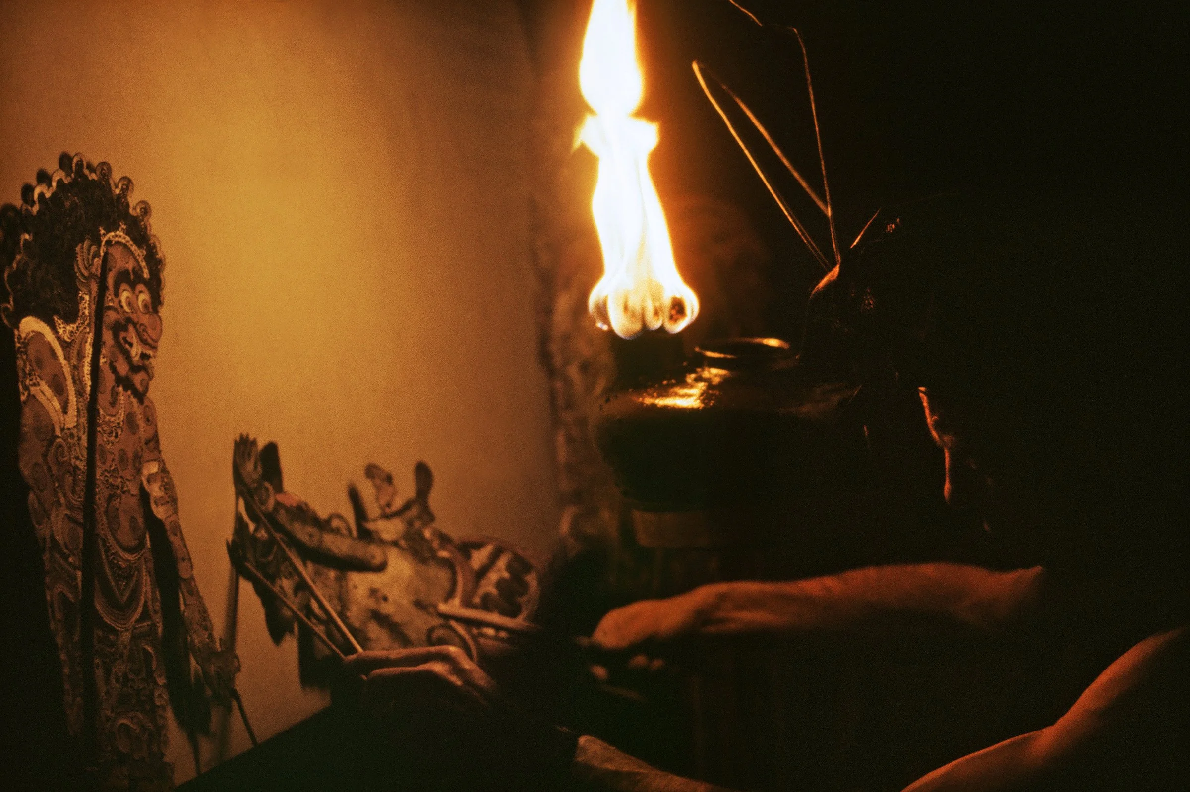 A person lighting an incense stick with a flame, with traditional Asian artwork visible on the wall in the background.
