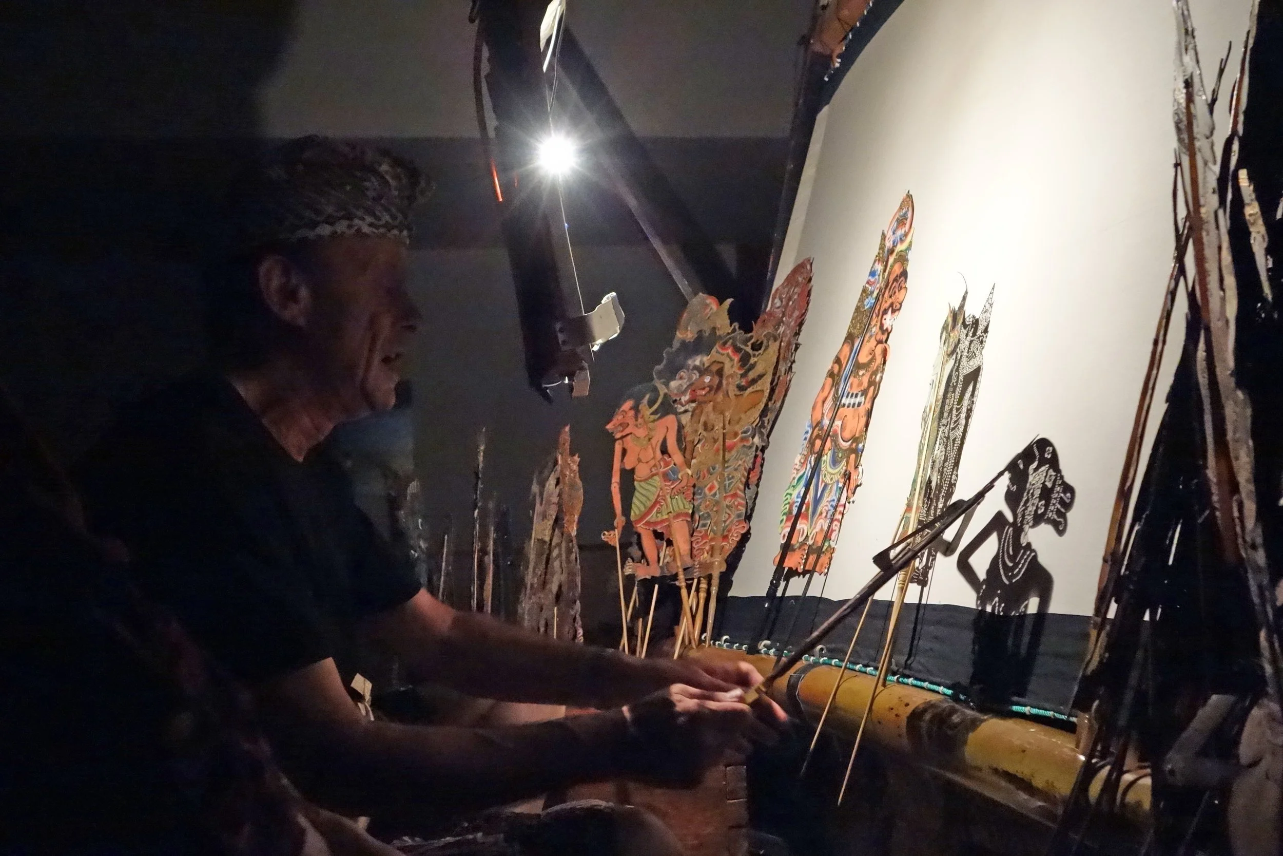 An artist creating traditional shadow puppets on a backlit screen in a dark room.