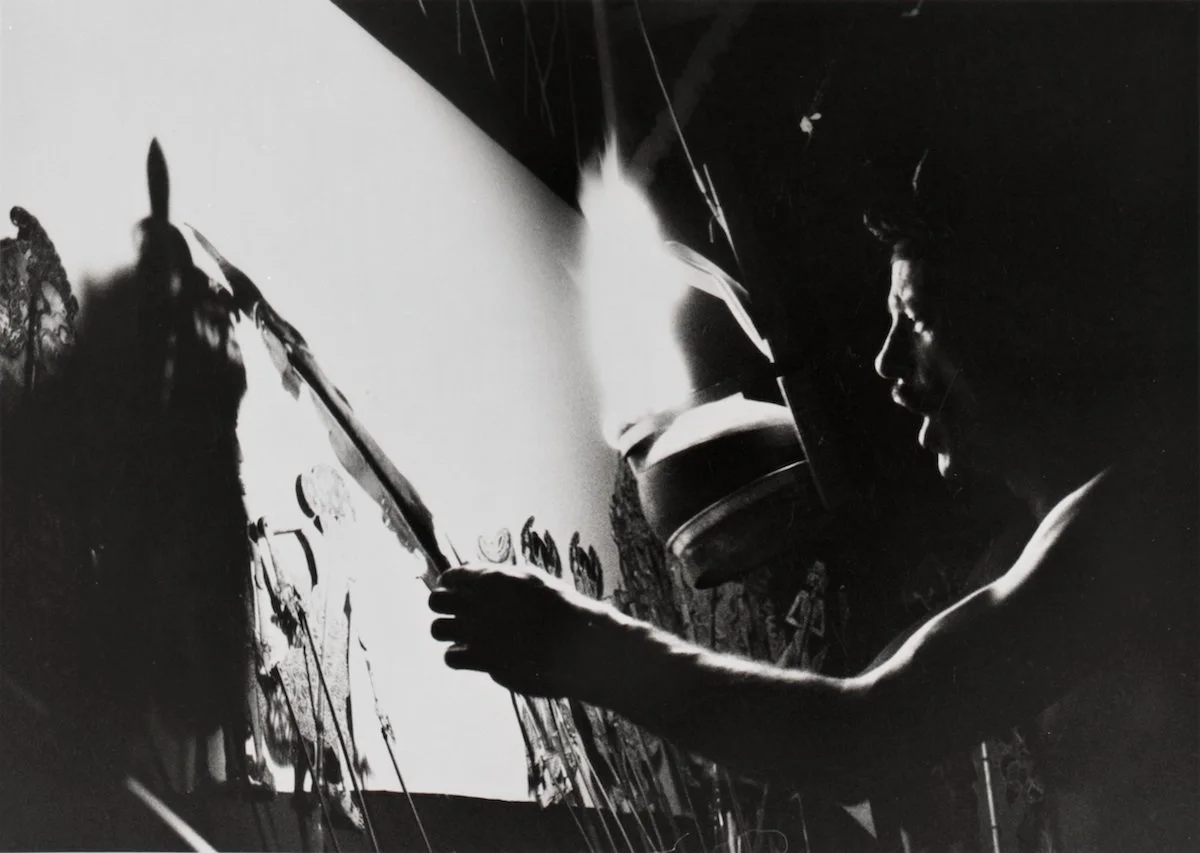 A person painting or drawing on a wall or canvas with a brush, using a light source to see the artwork, in black and white.