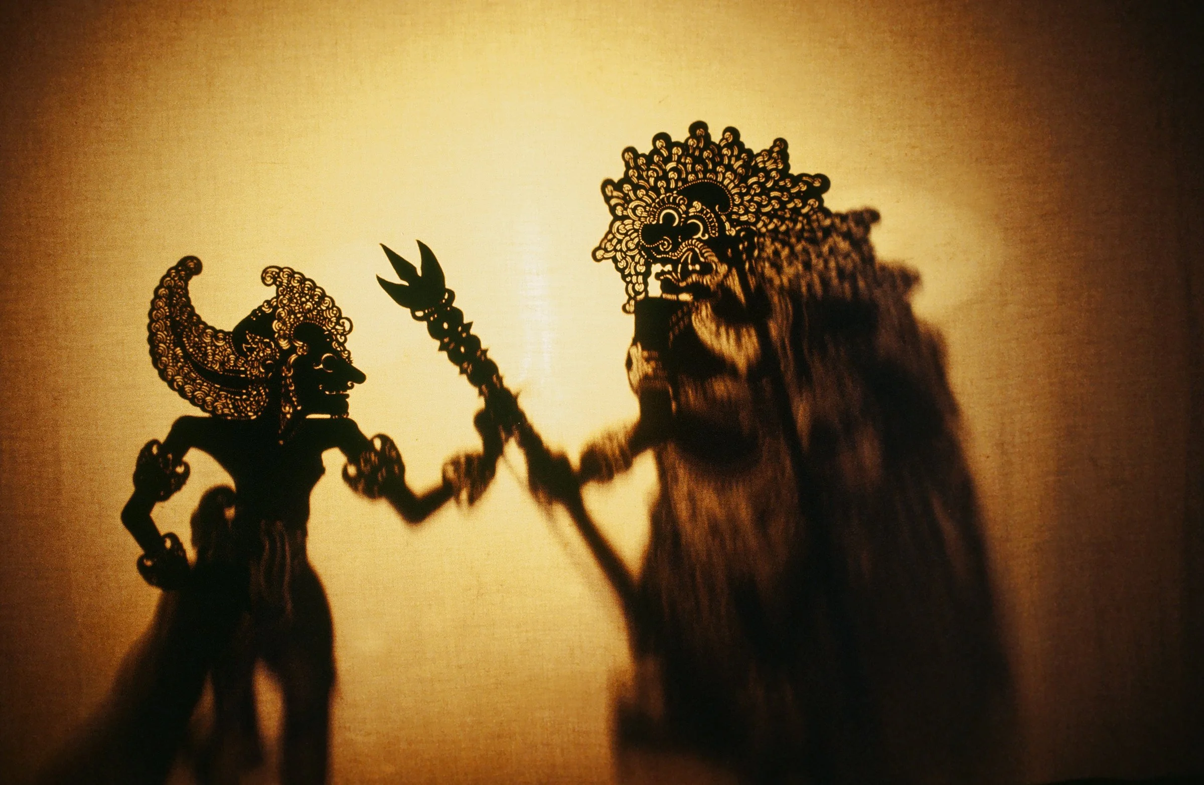 Shadow puppet depicting a mythological scene with two figures, one holding a trident, cast on a illuminated surface.