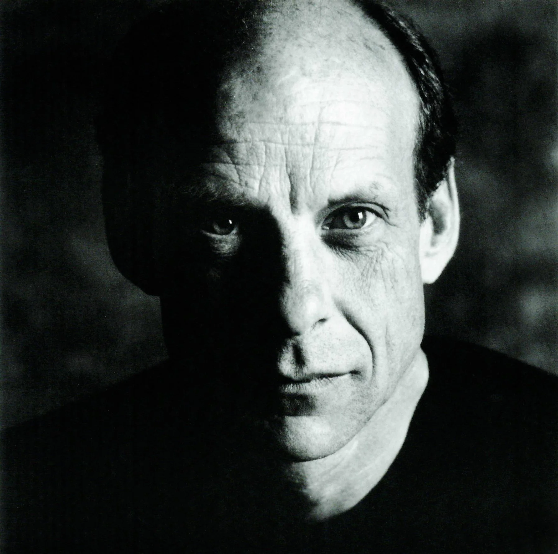 Black and white close-up portrait of a middle-aged man with a serious expression, short dark hair, and light-colored eyes.