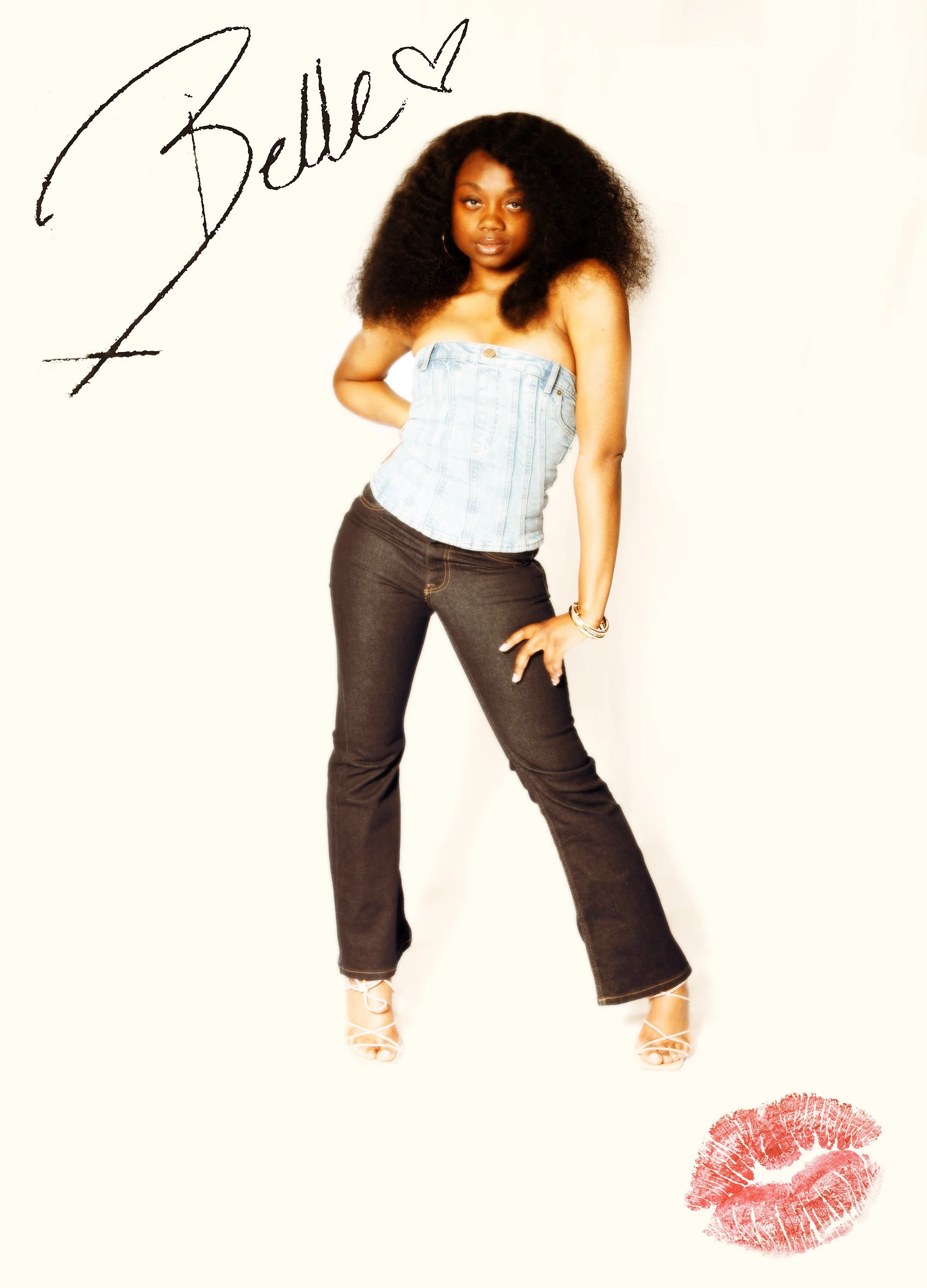 A woman with curly hair wearing a strapless denim top, dark jeans, and white high-heeled sandals, standing against a plain light background with a red lipstick kiss mark and the word 'Belie' written above in black handwritten style with a small heart