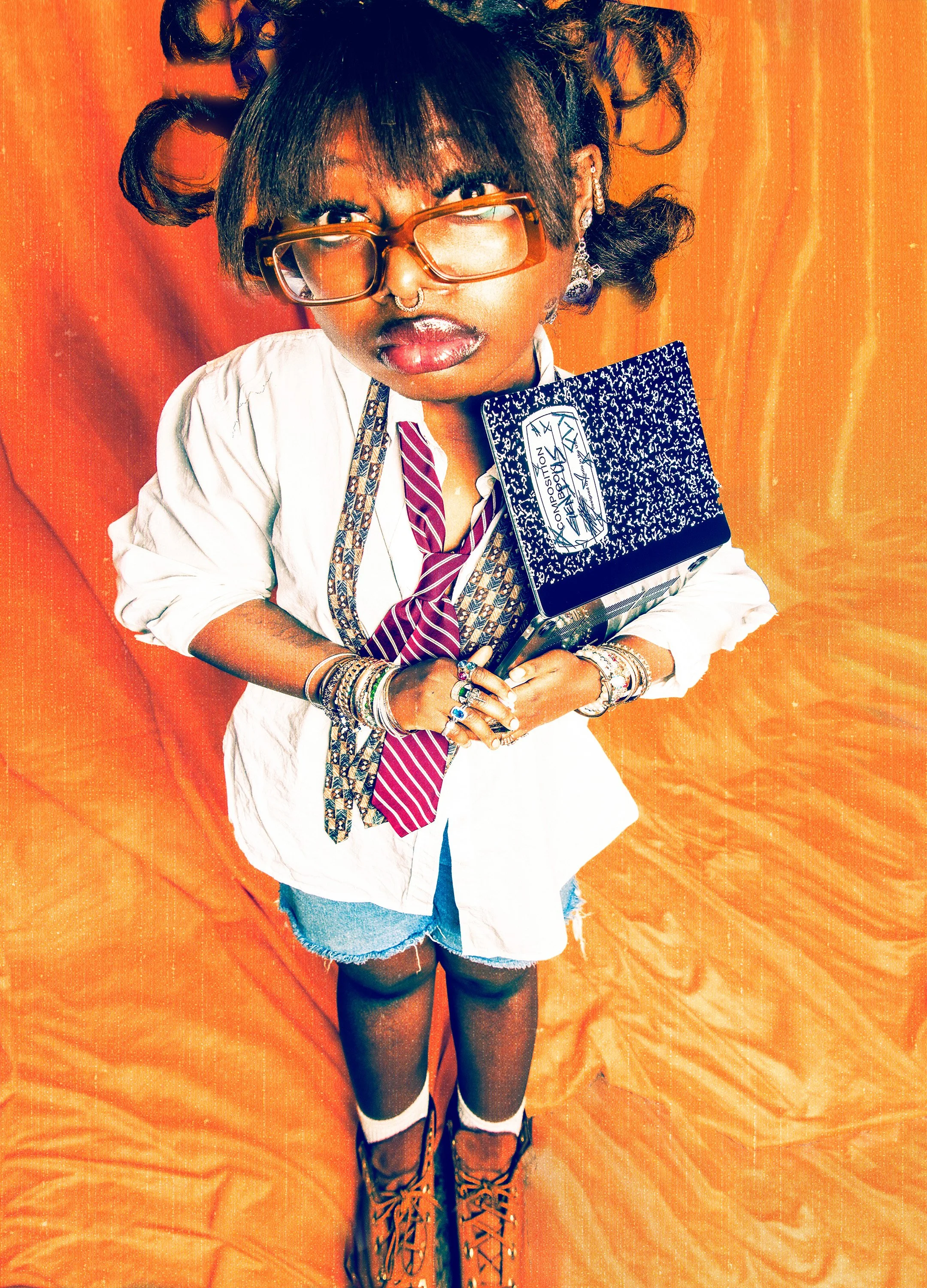 A person with medium brown skin, black curly hair styled with hair rollers, wearing oversized sunglasses, a nose ring, earrings, multiple bracelets and rings, a white shirt, a striped tie, denim shorts, black knee-high socks with white stripes, and t