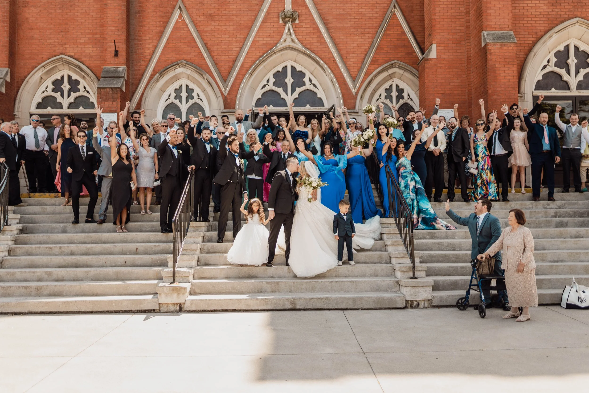 Group of people celebrating on front steps of a church, including a bride and groom, family, and friends at a wedding.