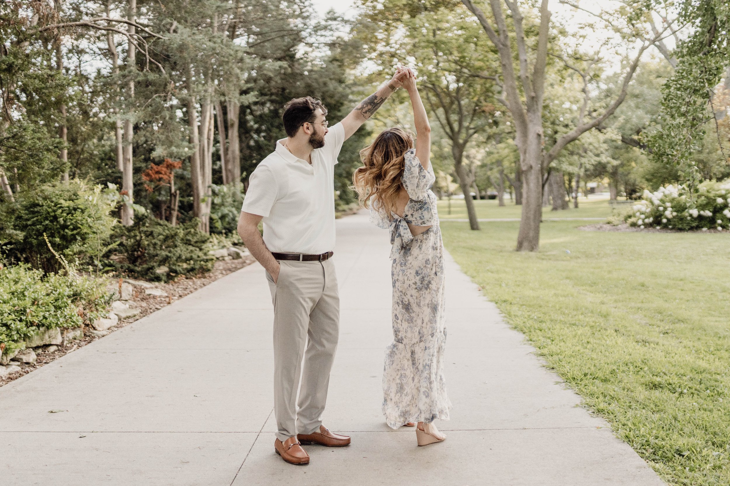 A couple dancing on a sidewalk in a park, surrounded by trees and greenery, during daytime.