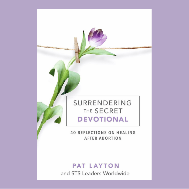 Book cover titled 'Surrendering the Secret Devotional' with a purple tulip and clothespin on a string, and subtitle '40 reflections on healing after abortion' by Pat Layton.