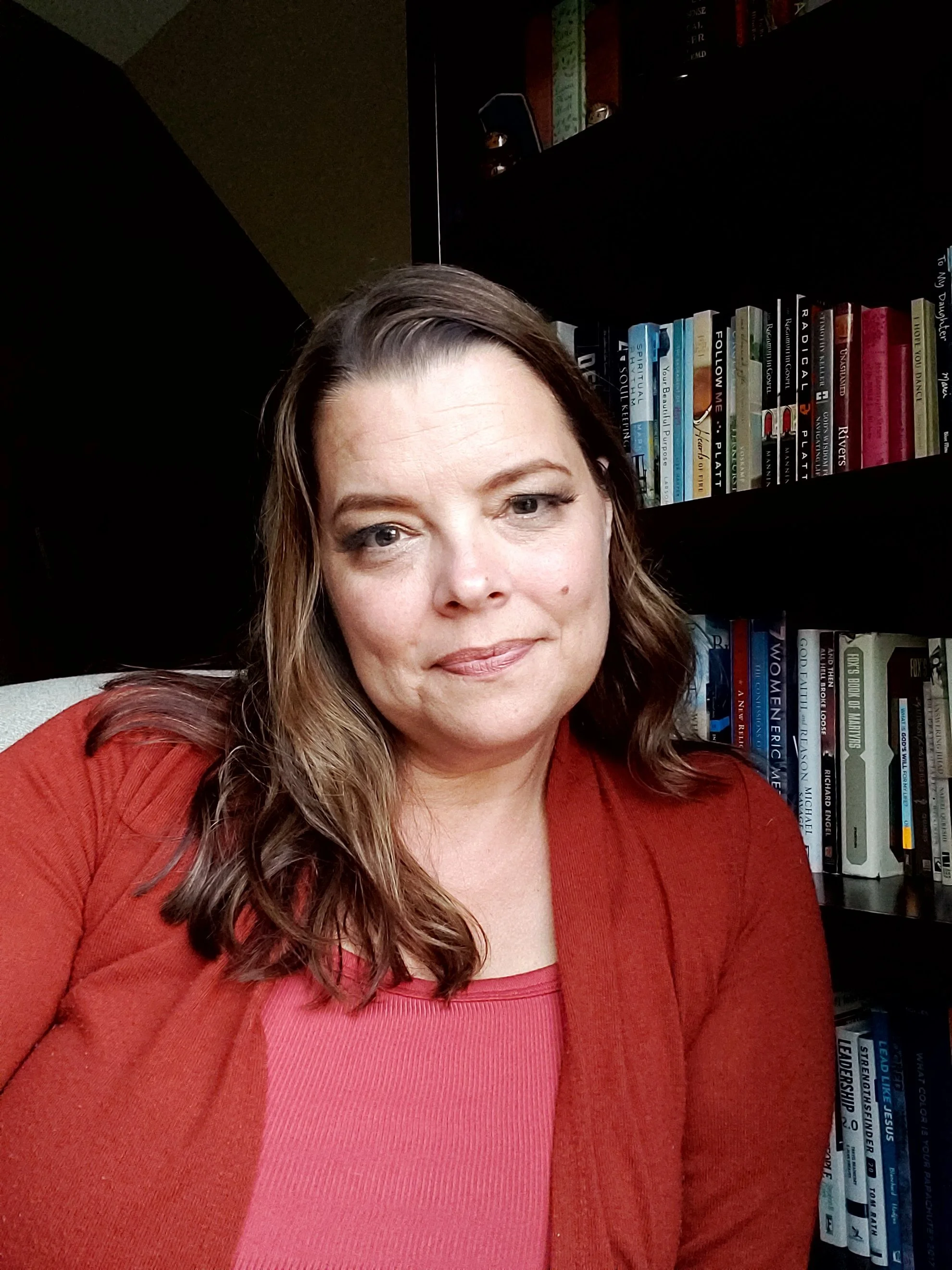 Danita Cummins sitting in a chair in her library next to her bookshelf.