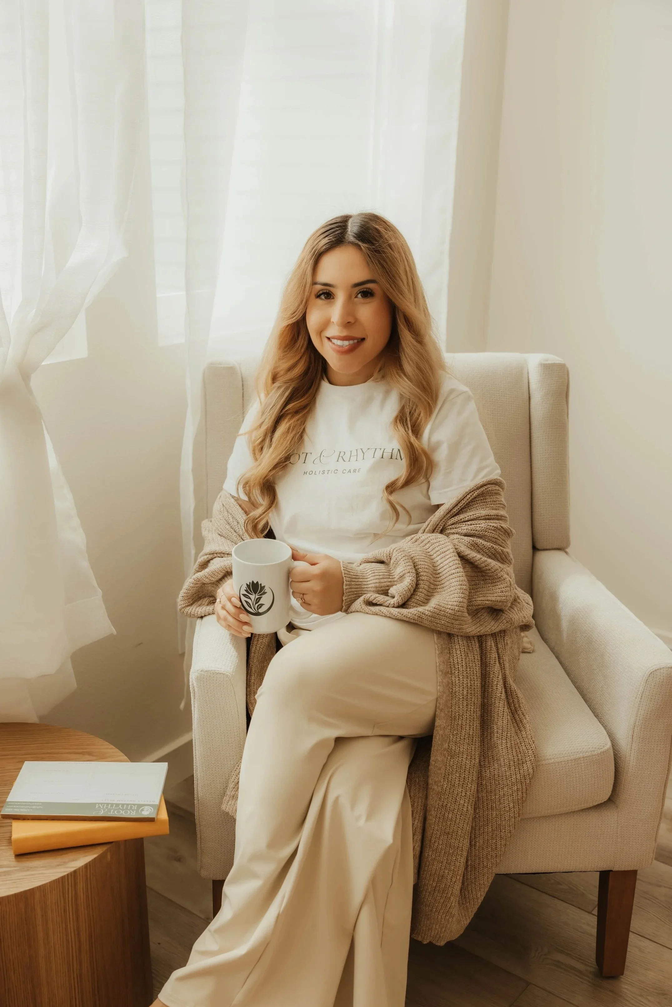 Dr. Salena Gallegos, OTD, OTR/L, founder of Root & Rhythm Holistic Care, sitting in a cozy wellness-inspired space with warm natural light, coffee in hand, and a grounded, welcoming presence.
