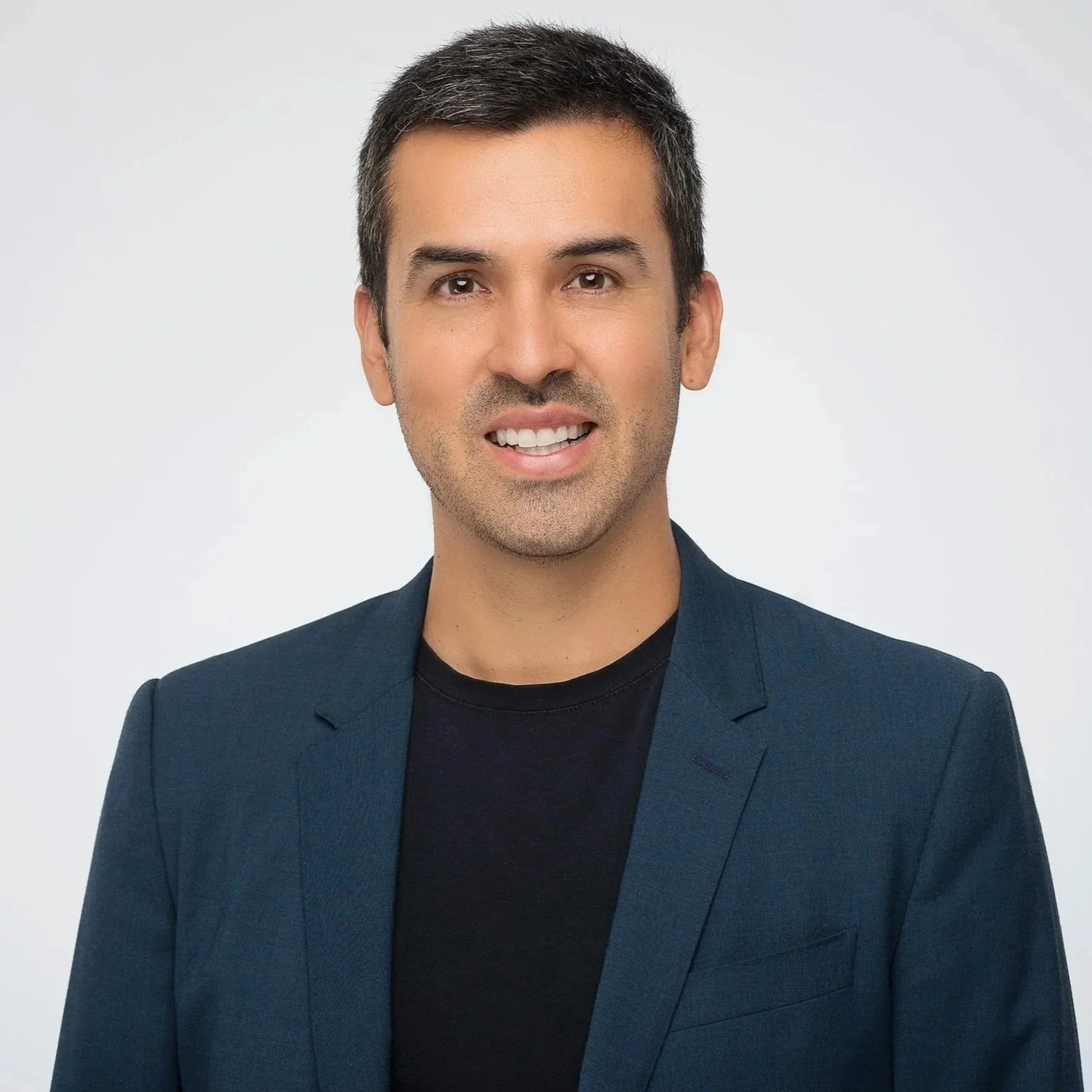 Foto retrato de profesional en estudio con ligera sonrisa, fondo gris y blazer casual.