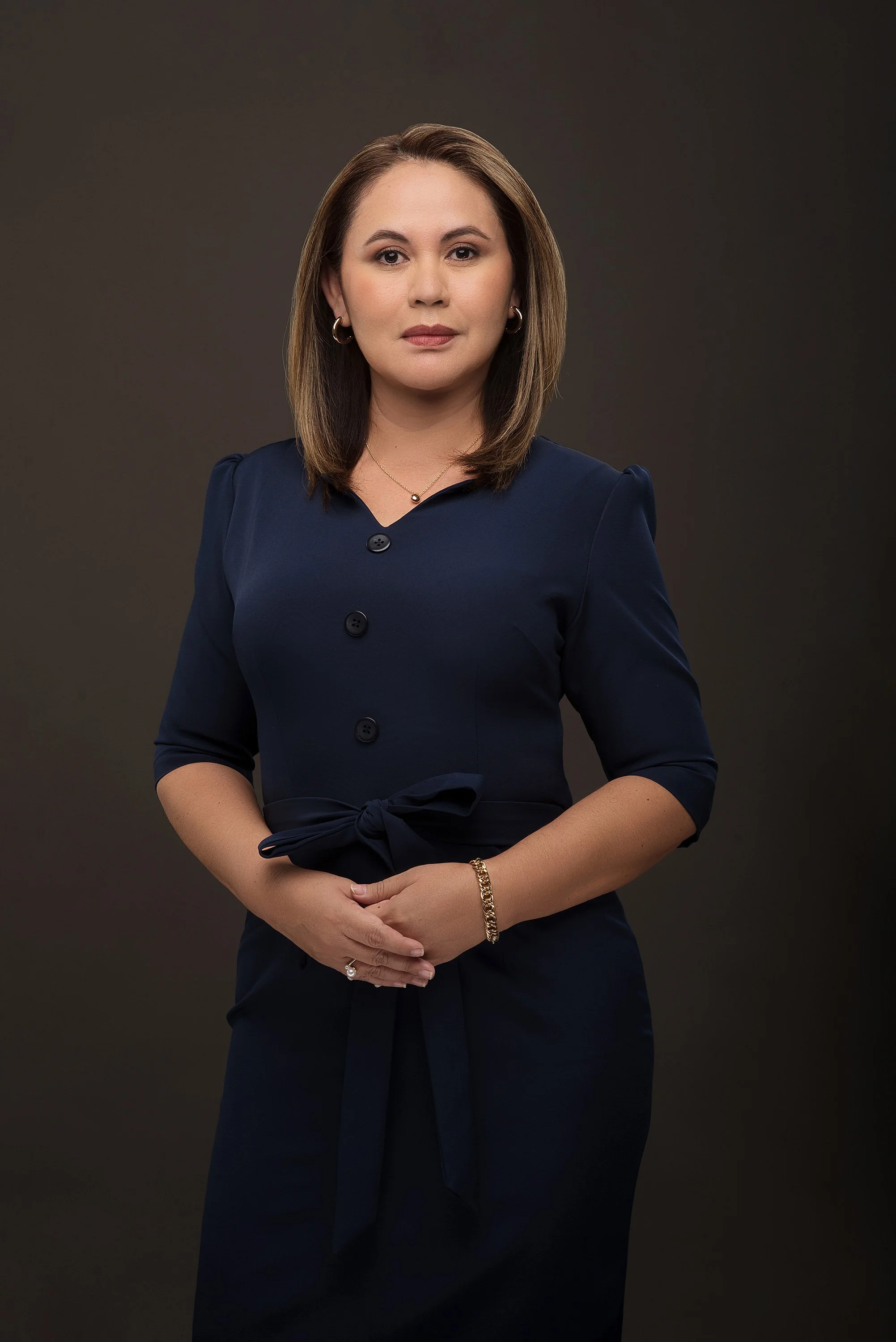 Fotografía en estudio de una abogada con expresión segura y elegante. Fondo gris oscuro, luz precisa y dirección cuidada que refuerzan su presencia profesional y autoridad en el ámbito legal o corporativo.