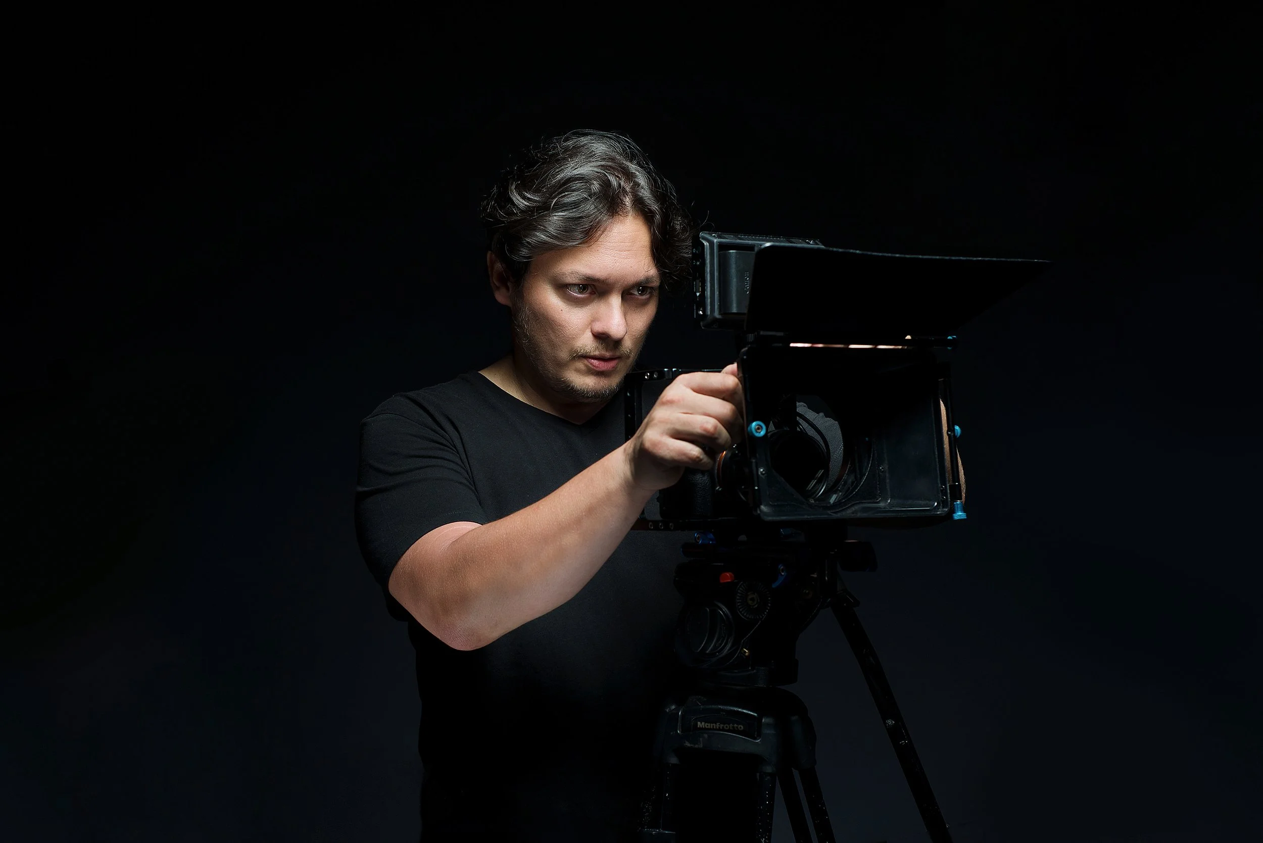 Retrato profesional de un cineasta en estudio, sosteniendo su cámara con actitud segura y creativa. Fotografía que transmite liderazgo, visión artística y dominio técnico, ideal para perfiles del sector audiovisual o cultural.