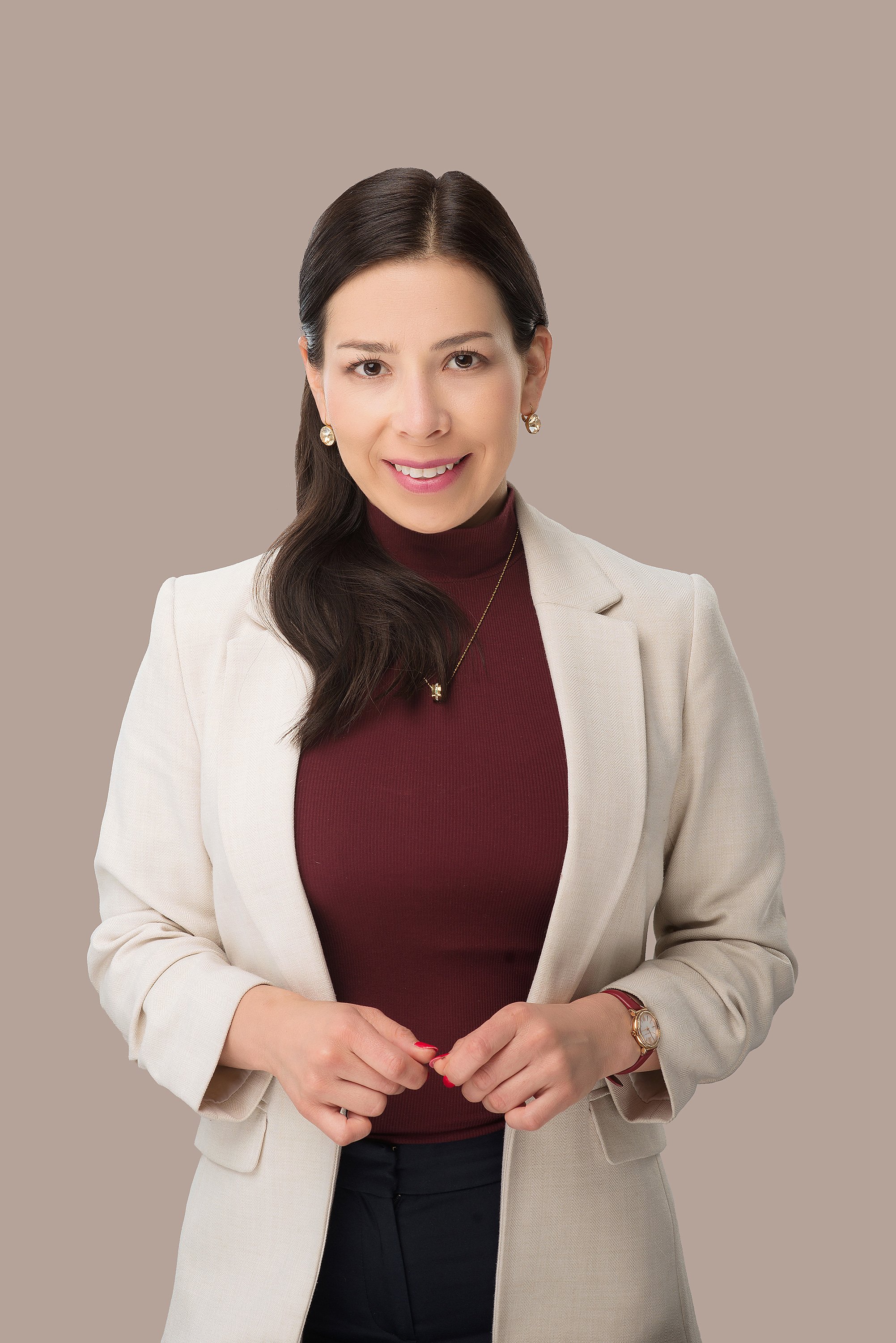 Fotografía profesional en estudio, persona de medio cuerpo con ligera sonrisa, fondo beige y vestimenta casual.